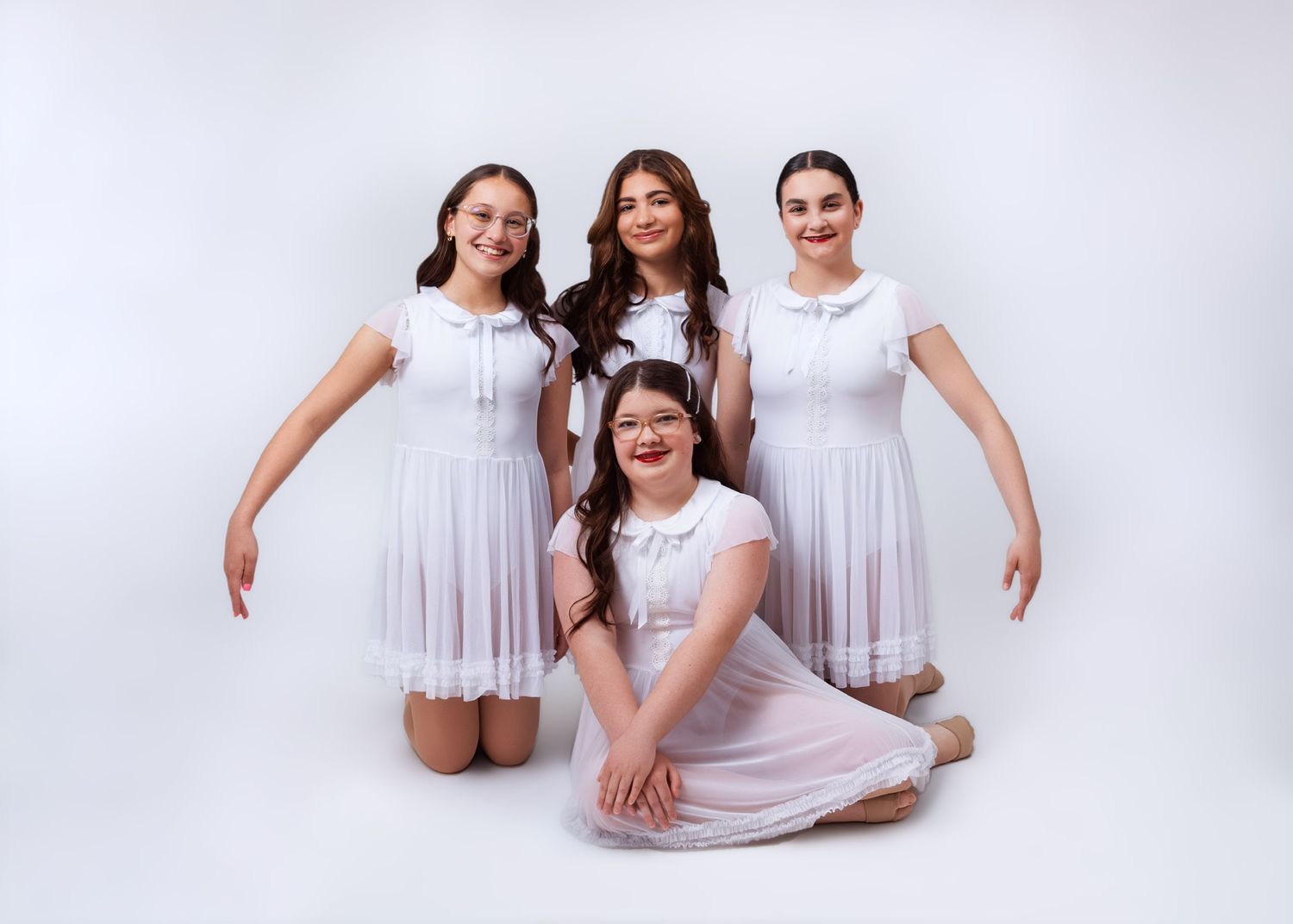 Four girls in matching white dresses pose together for a dance studio group portrait photo.