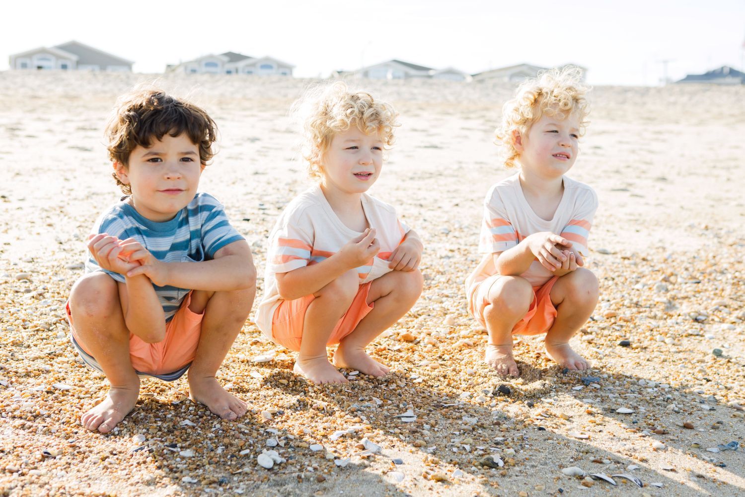 Three young children squatting on a sandy beach in summer.