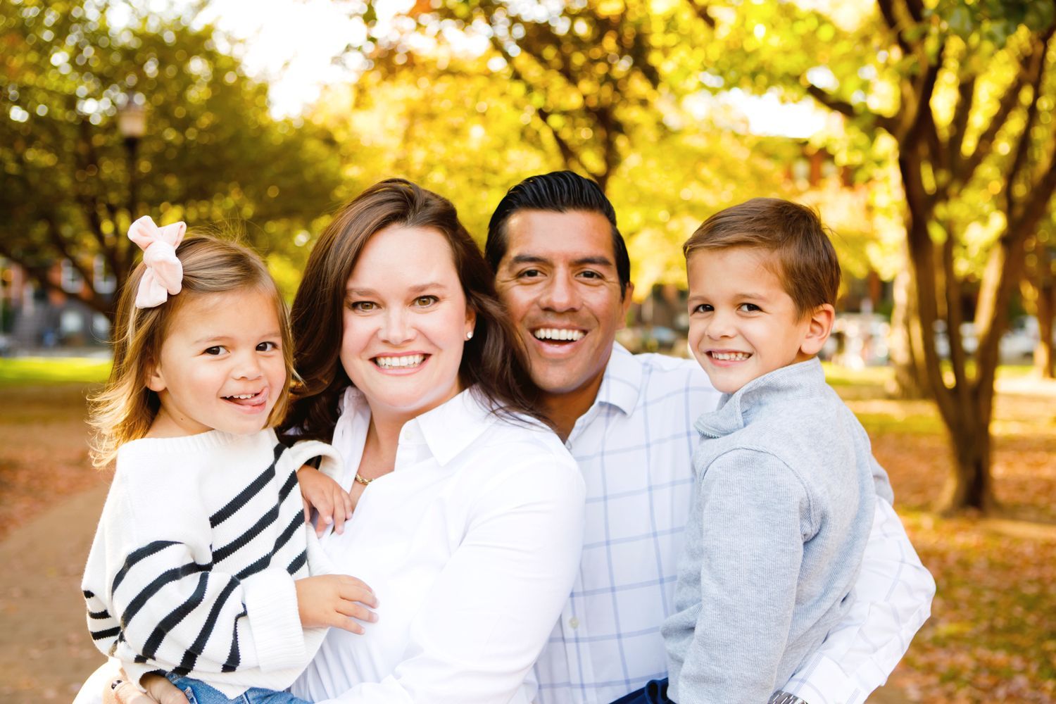 Smiling family of four posing outdoors in an autumn park.