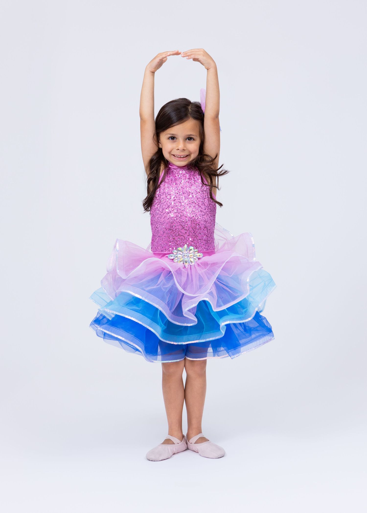 Young girl in pink sequined and blue tiered tutu dance dress posing on white background.