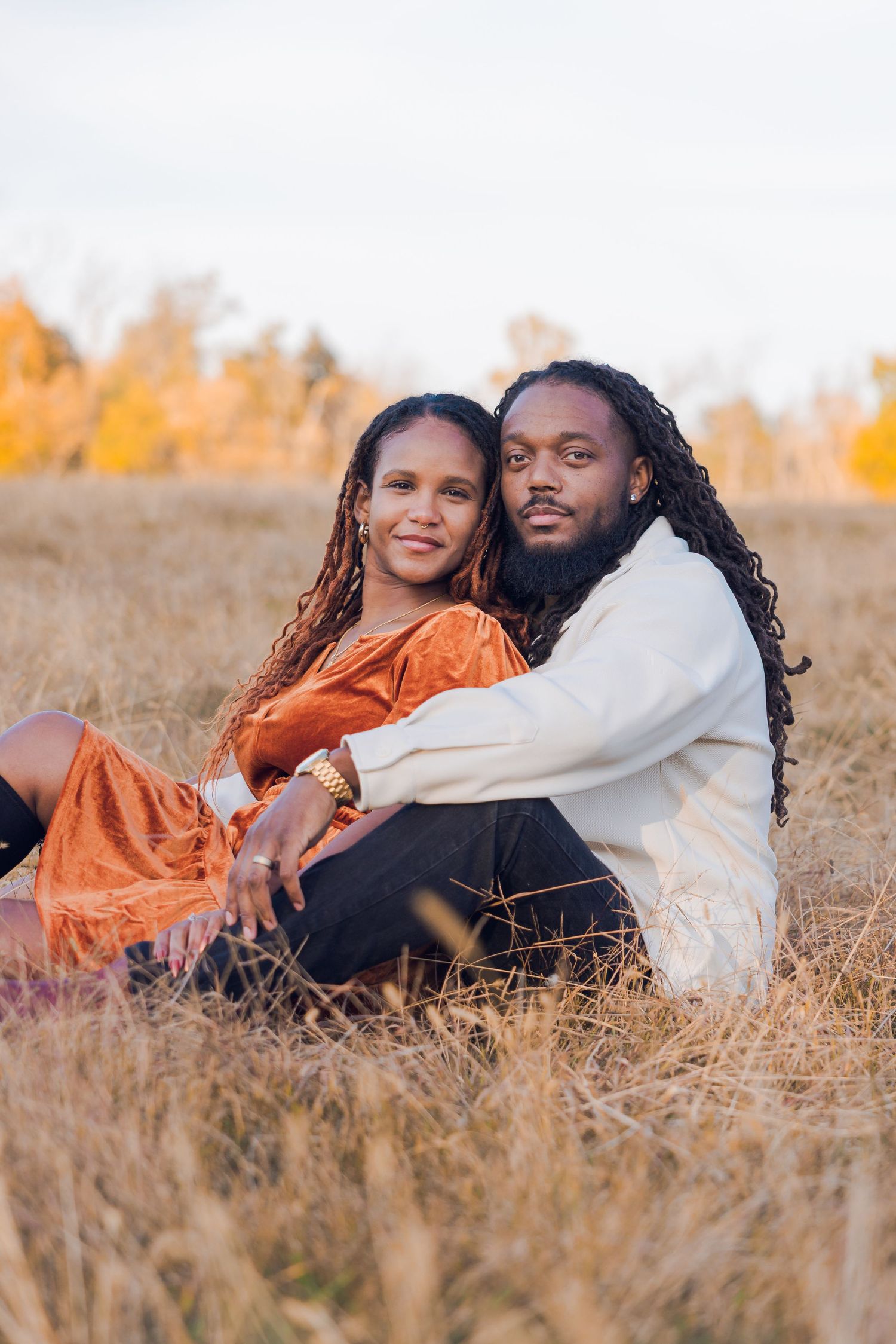 Loving couple sitting together in a golden autumn field, man embracing woman in orange dress.