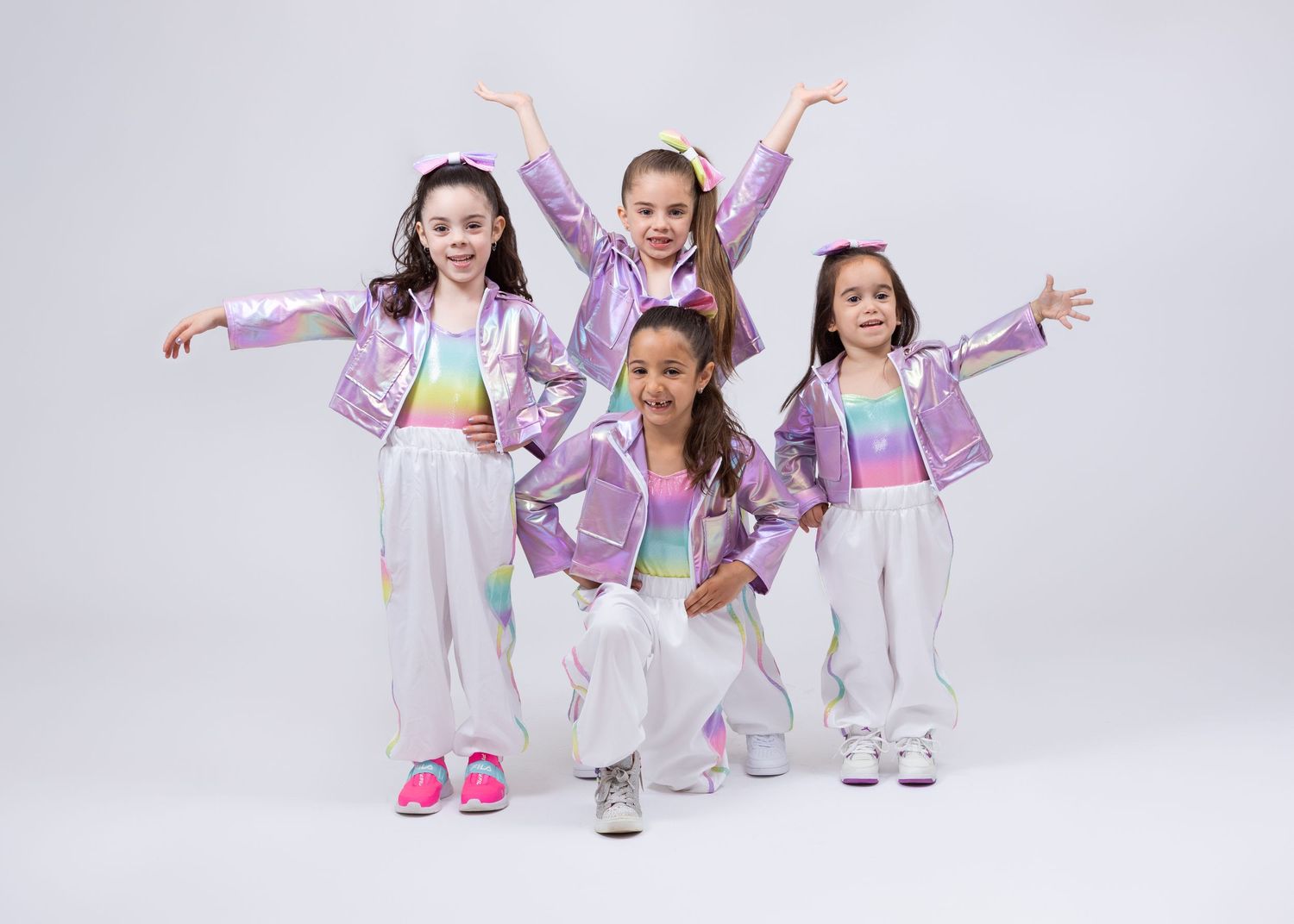 Group of four girls in matching iridescent purple jackets and white pants pose in dance formation.