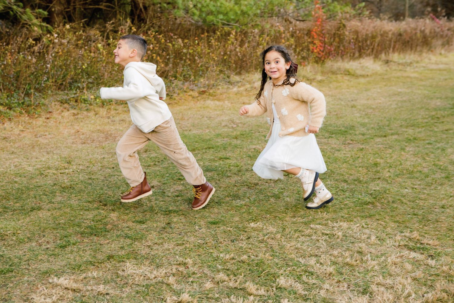 Two children running and playing together on a grassy field during an outdoor photo session.