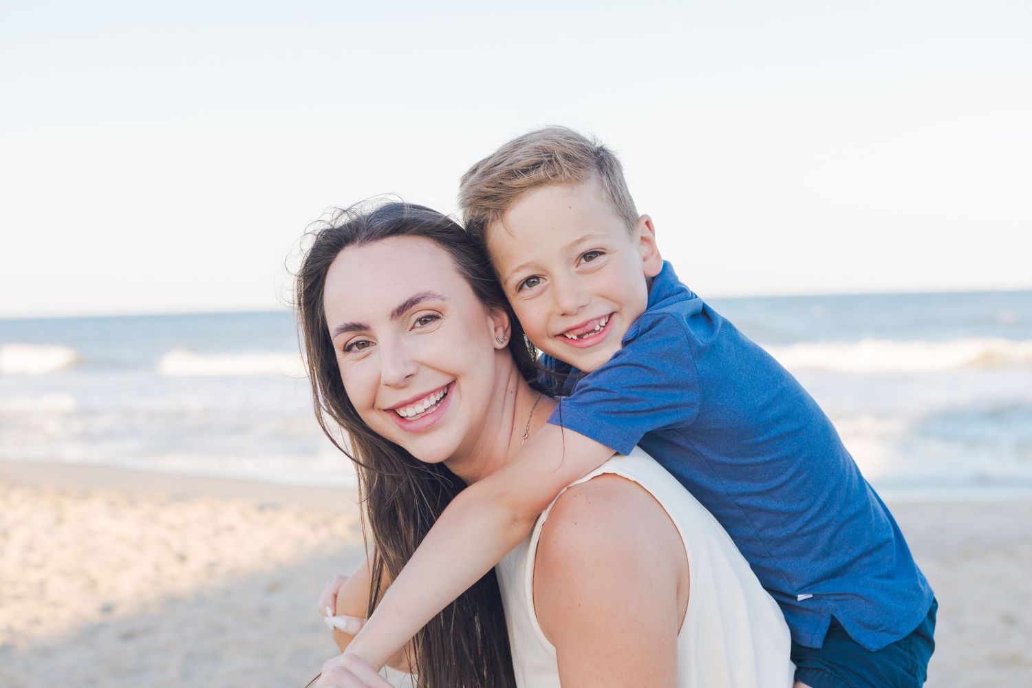 Happy mother and young son smiling together on a beautiful sunny beach by the ocean.