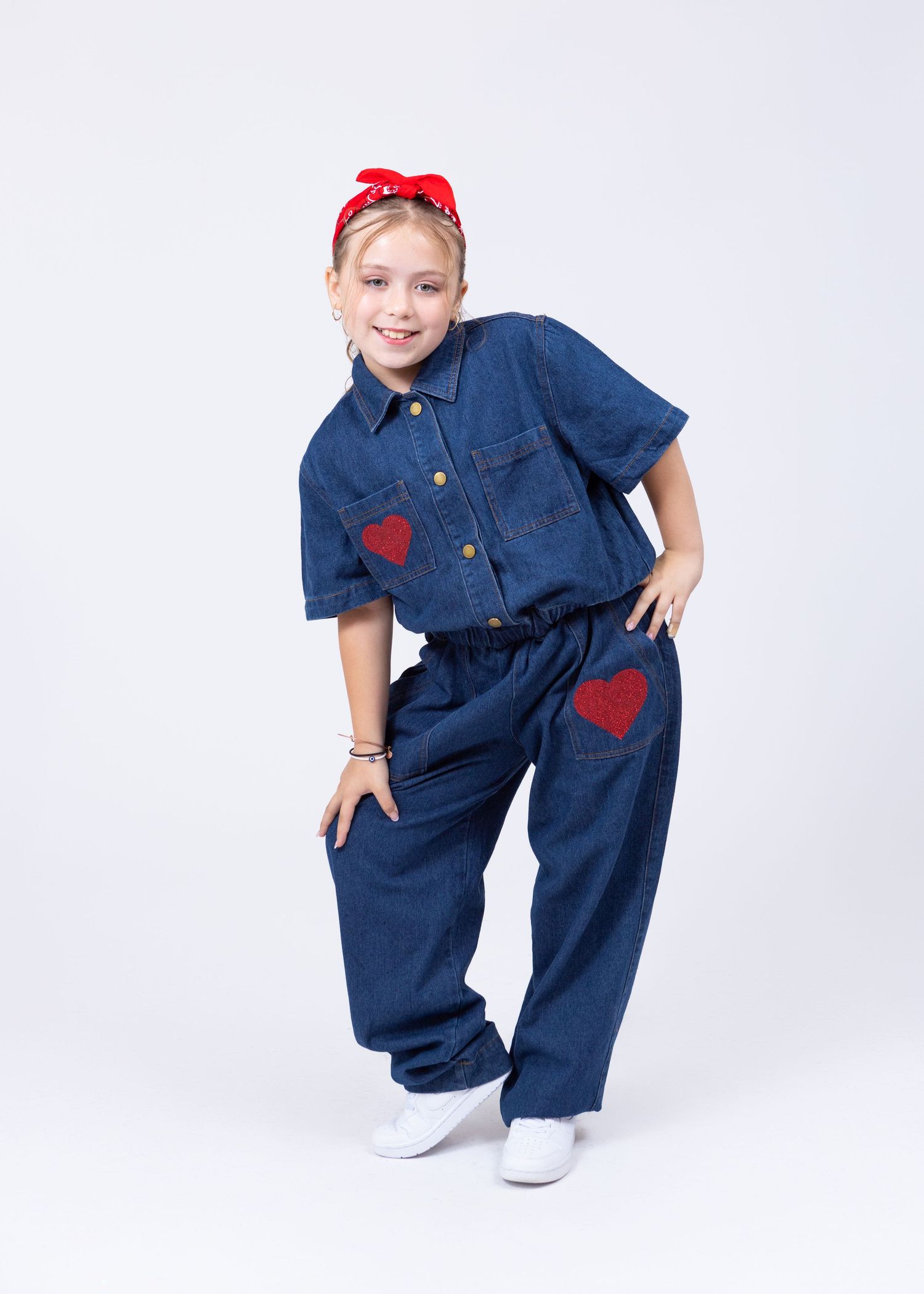 A young girl in a denim outfit with red heart patches and red headband strikes a dance pose.