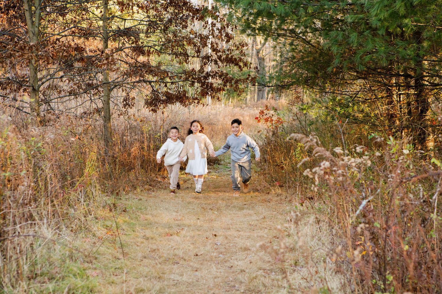 Three children running hand-in-hand down a scenic autumn forest trail.