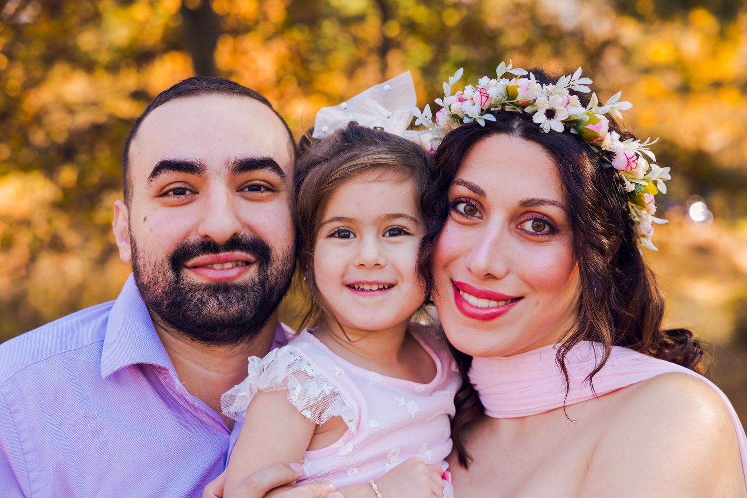 Happy family of three smiling together outdoors in autumn with colorful fall foliage.