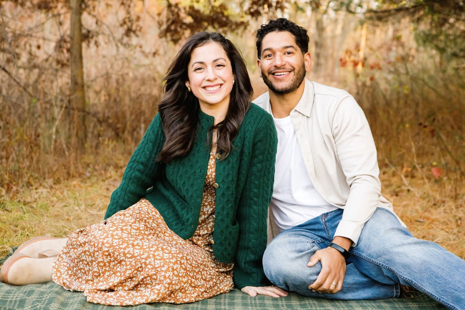 Smiling couple sitting together on a plaid blanket in a beautiful autumn outdoor setting.