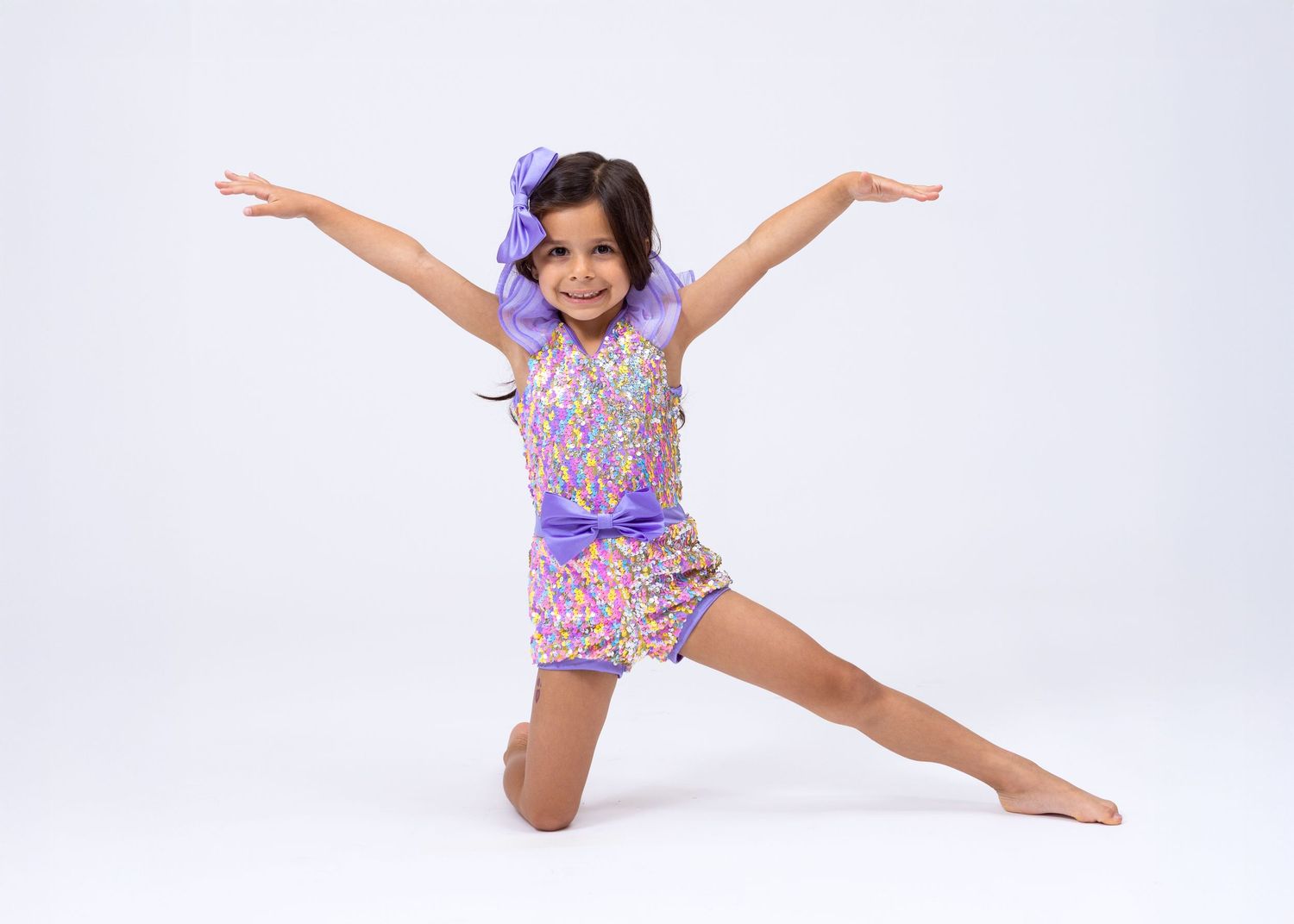 Young girl in purple sequined dance costume performing a split pose on white background.