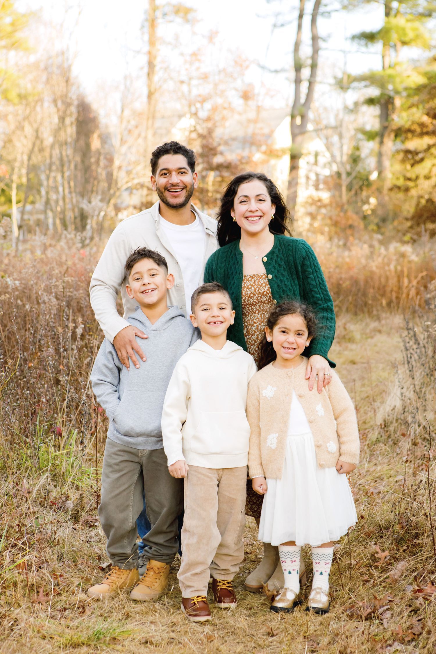 Family of five smiling together on an autumn woodland path, parents with three young children.