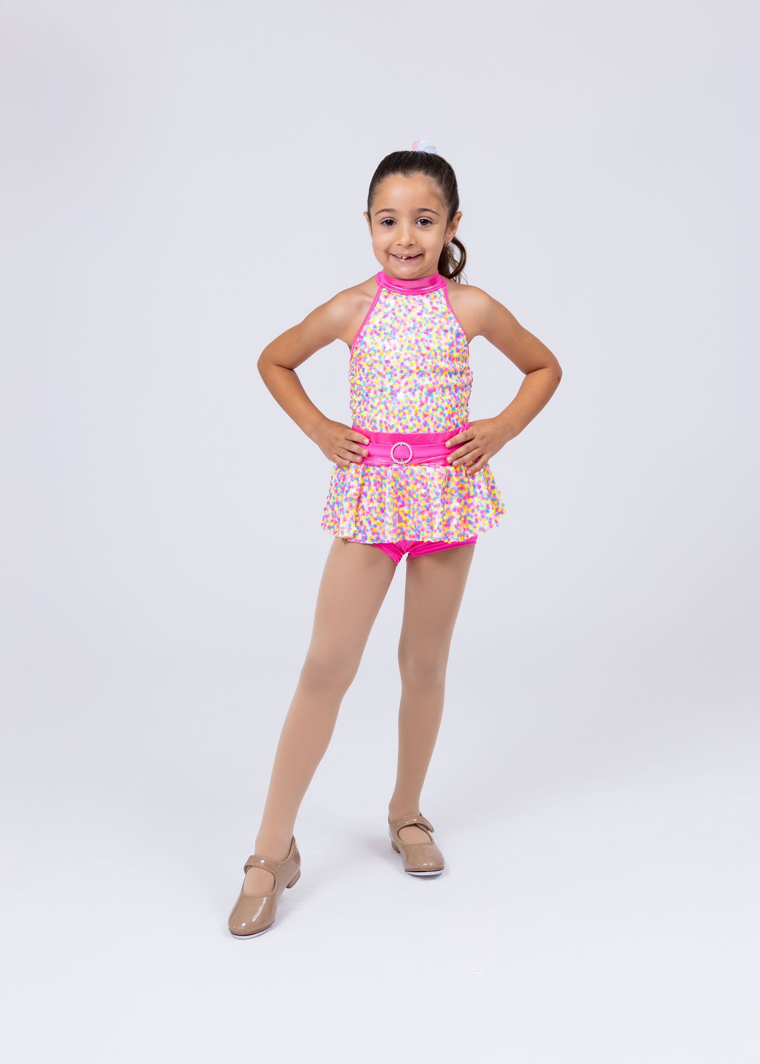 Young girl in pink floral dance costume with skirt poses confidently in a studio portrait.