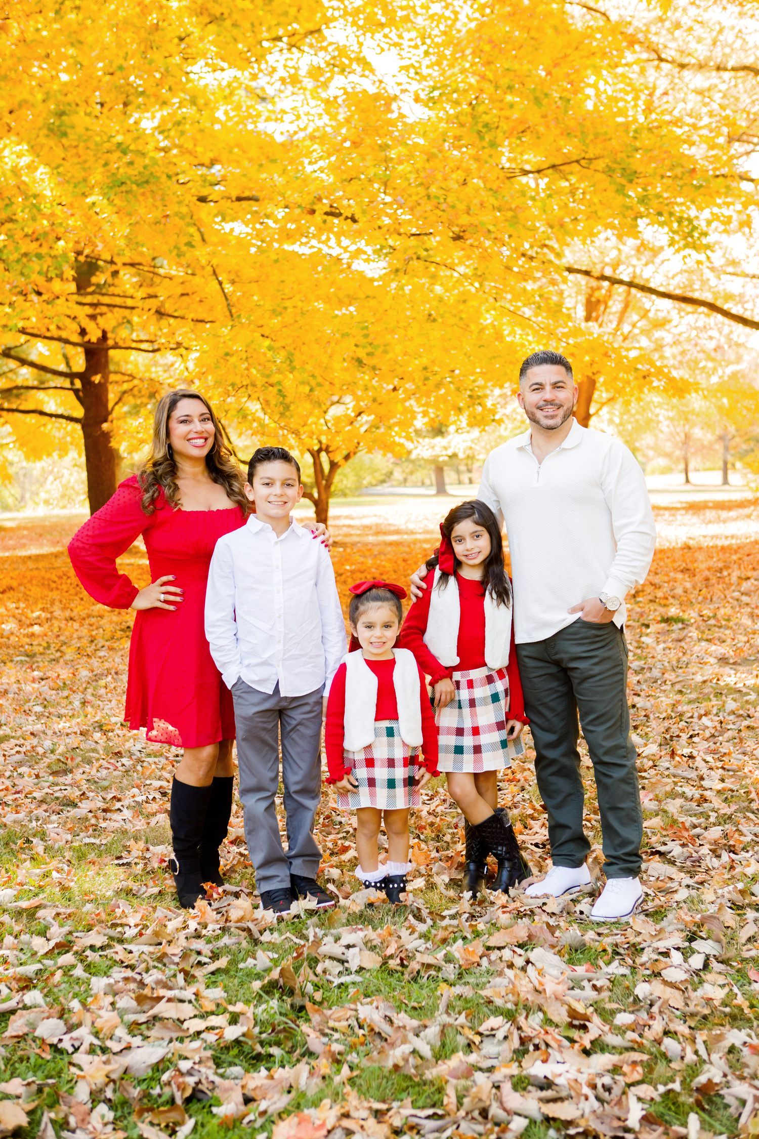 Family of five in red and white outfits posing under vibrant yellow autumn trees.