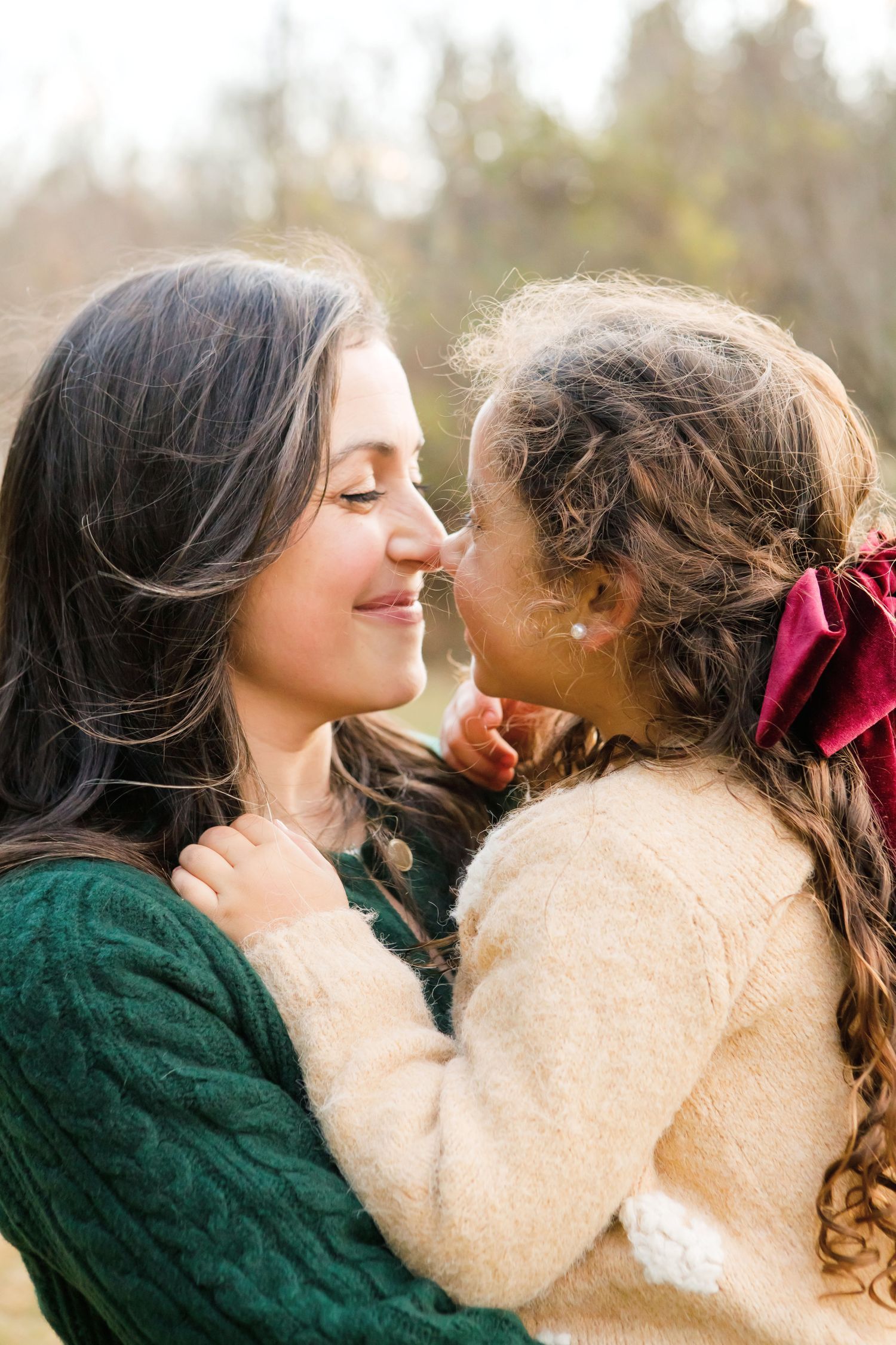 Mother and young daughter sharing a tender nose-to-nose moment outdoors.