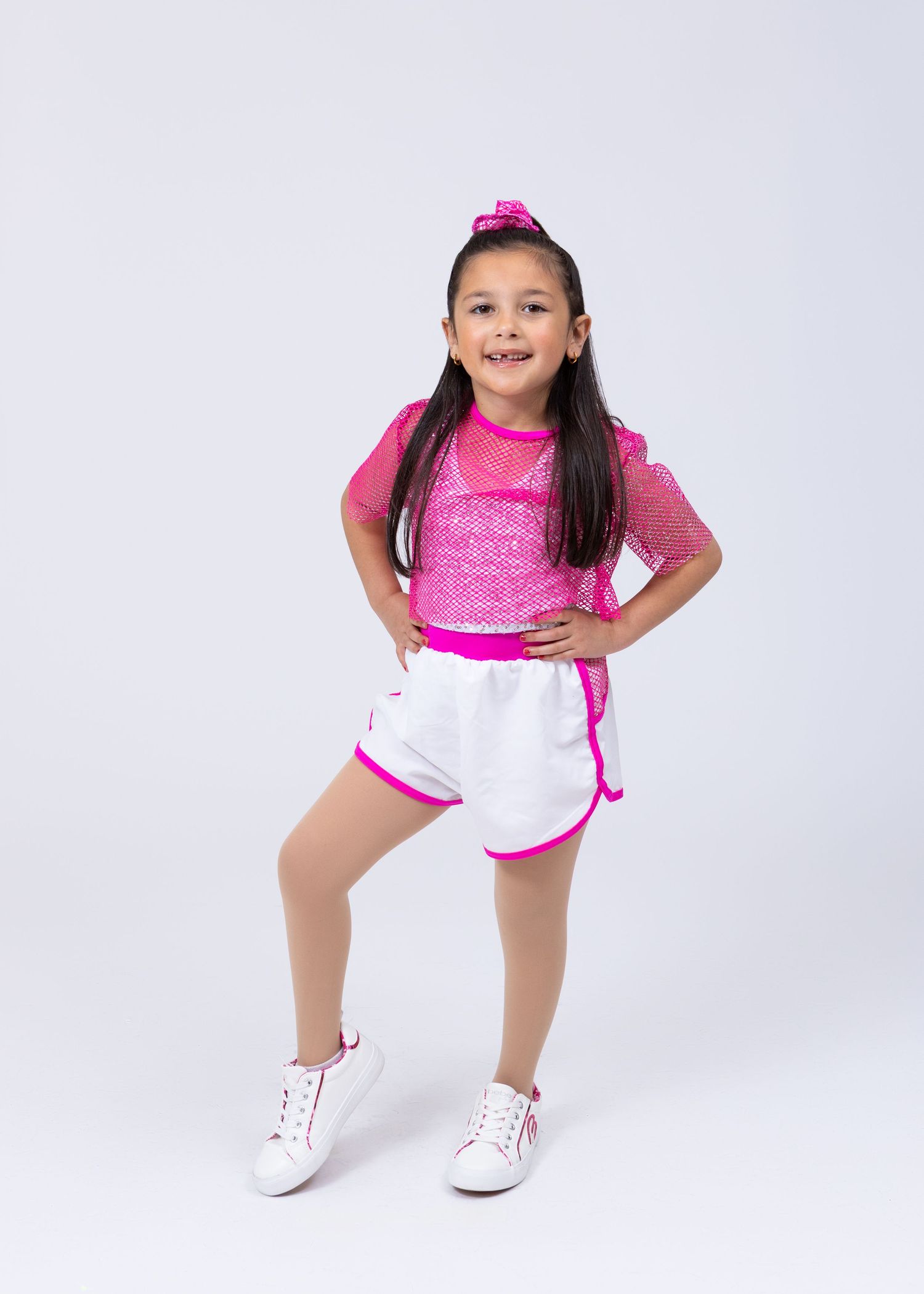 Young girl in pink sequin top and white shorts with pink trim poses confidently in dance costume.