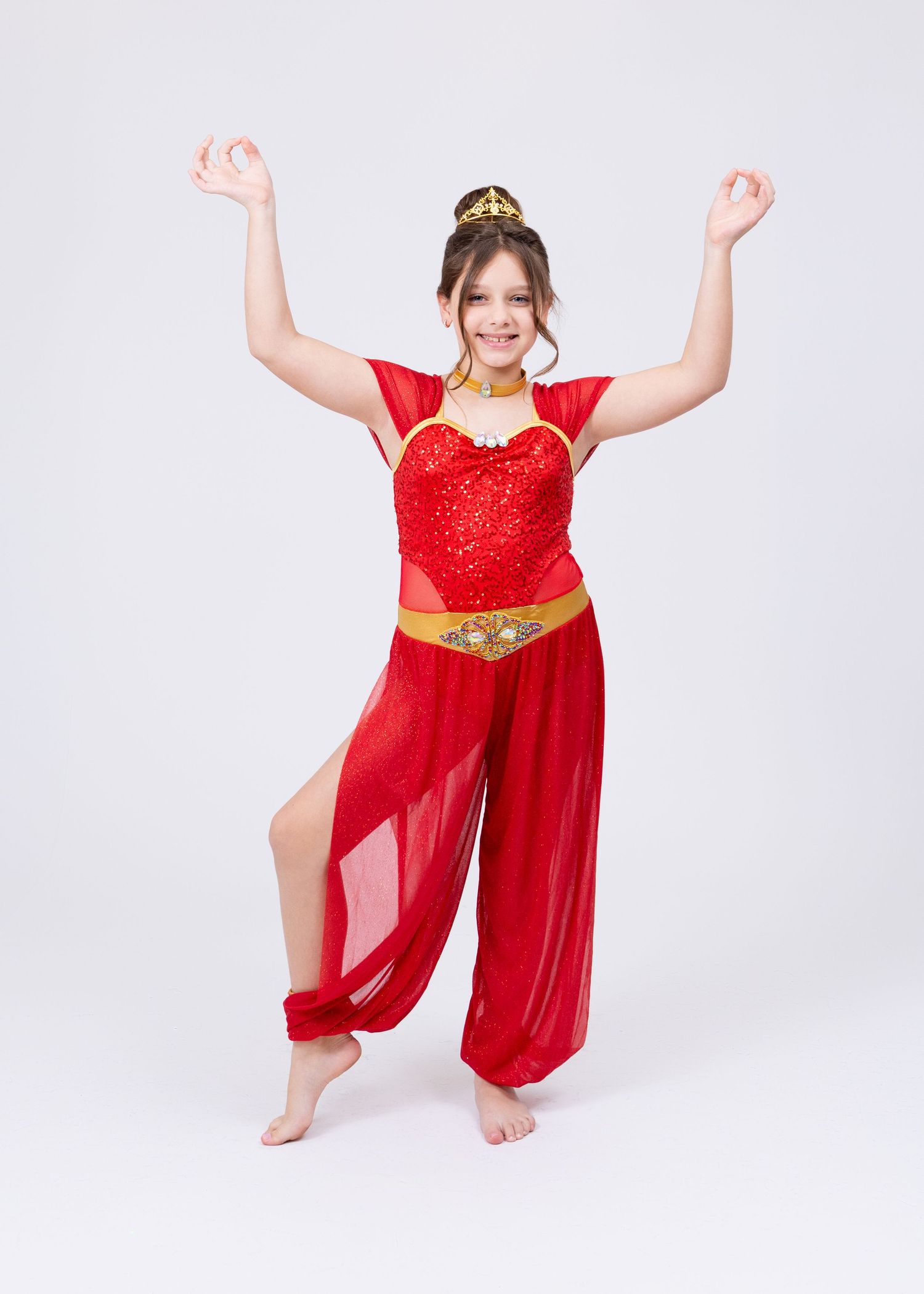 Young girl in red sequin Arabian dance costume with gold belt performs with arms raised.