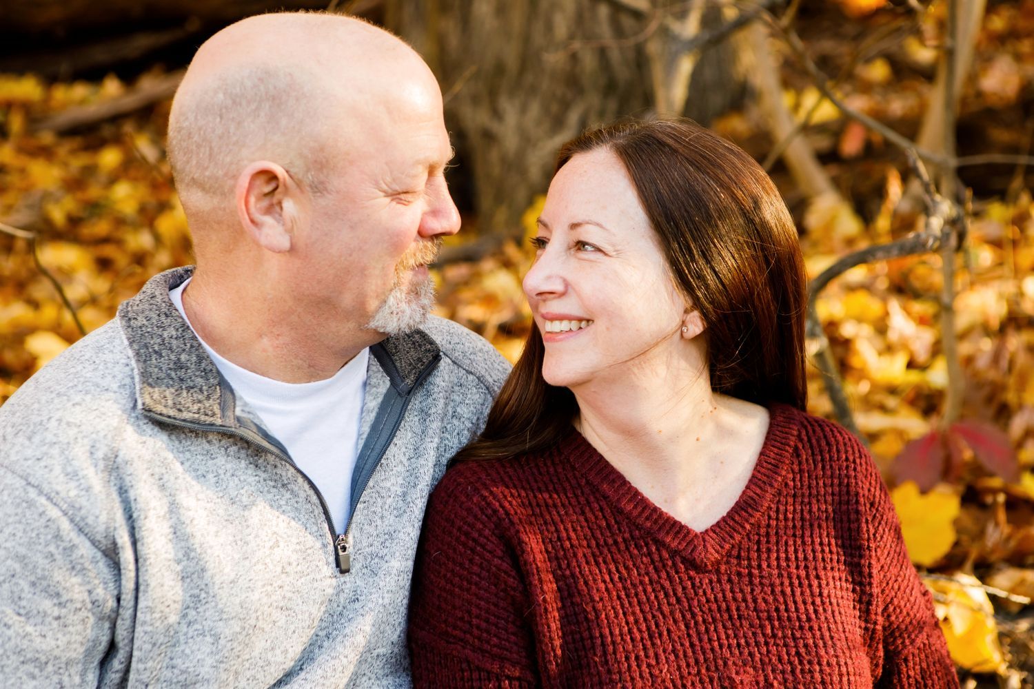 Smiling couple gazing at each other surrounded by golden fall foliage outdoors.