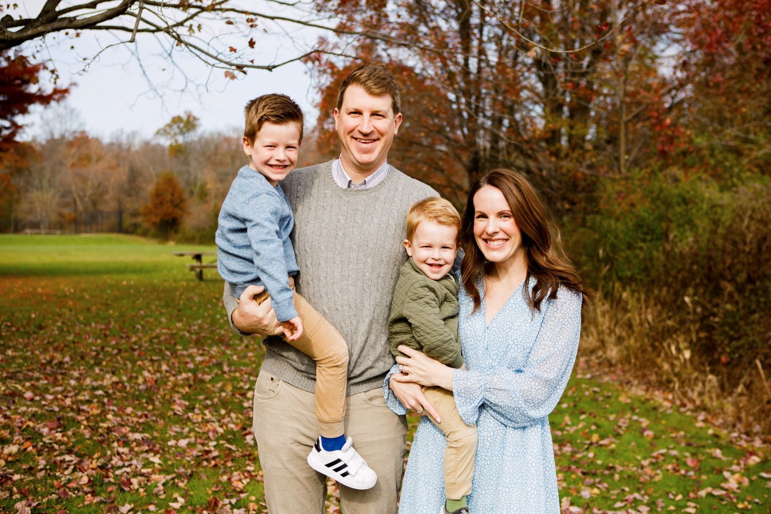 Happy family of four with two young boys poses in colorful autumn park setting outdoors.