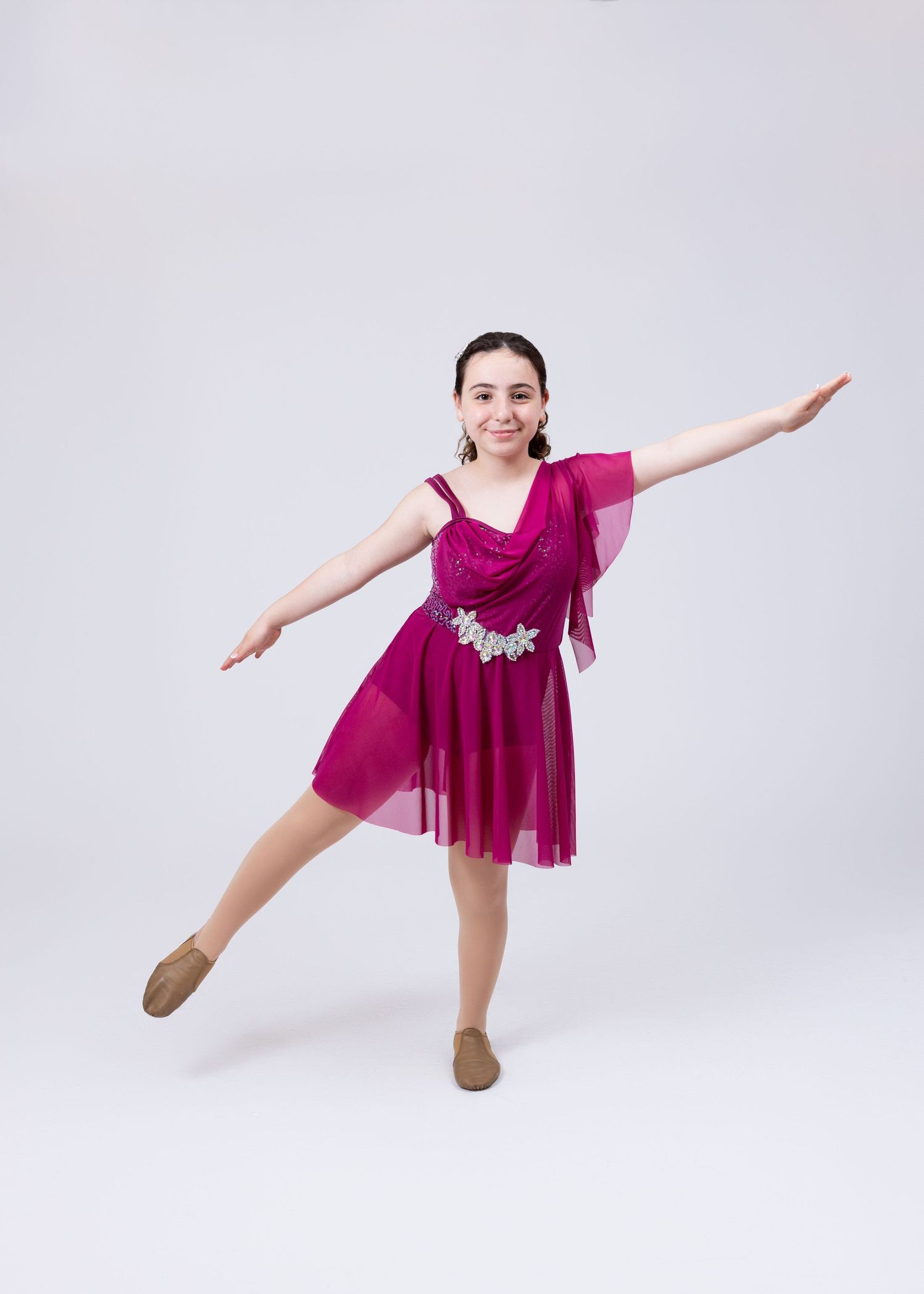 A teenage girl in a magenta dance dress with floral detail performs an elegant arabesque pose.