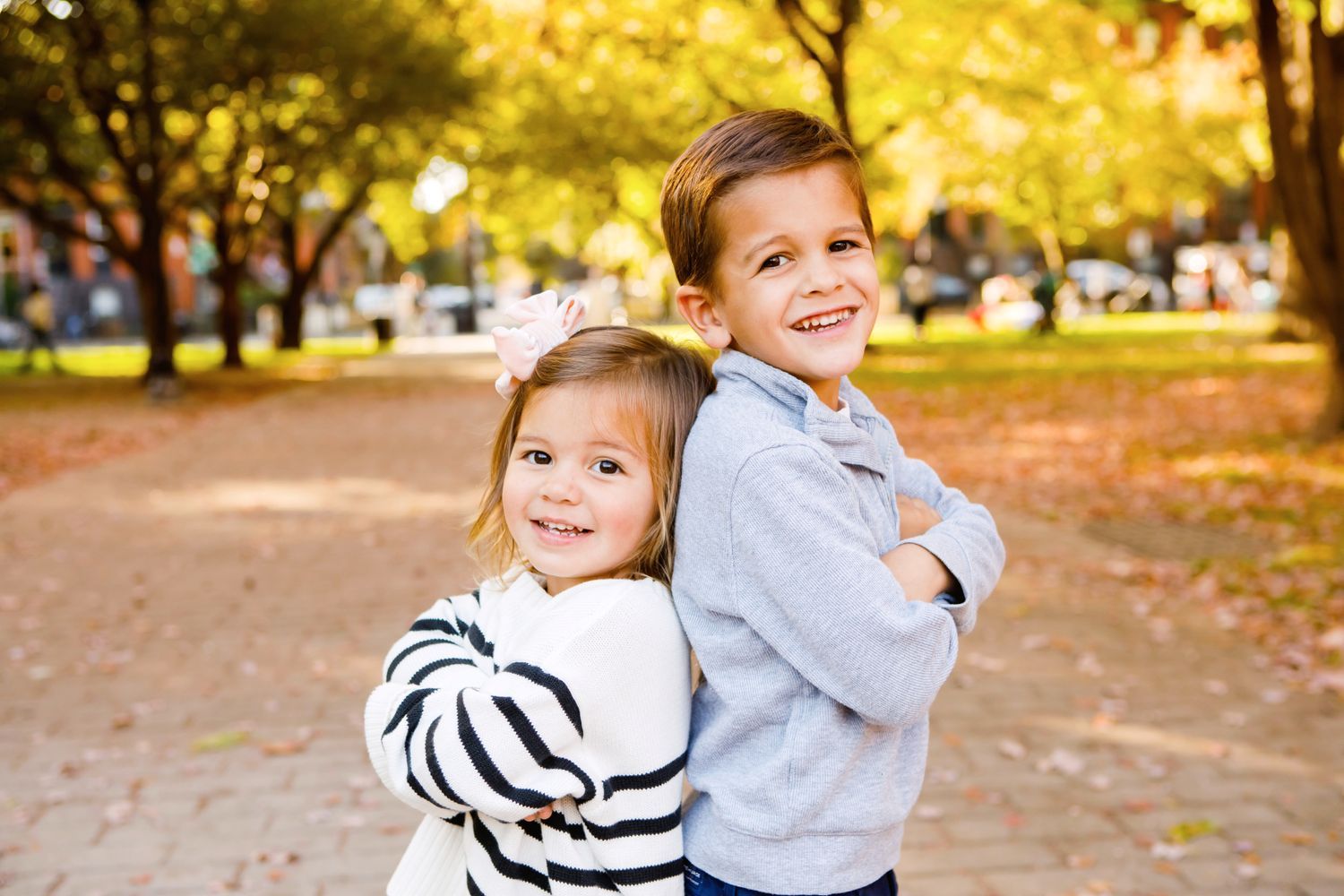 Young siblings hugging back-to-back in a fall park setting.
