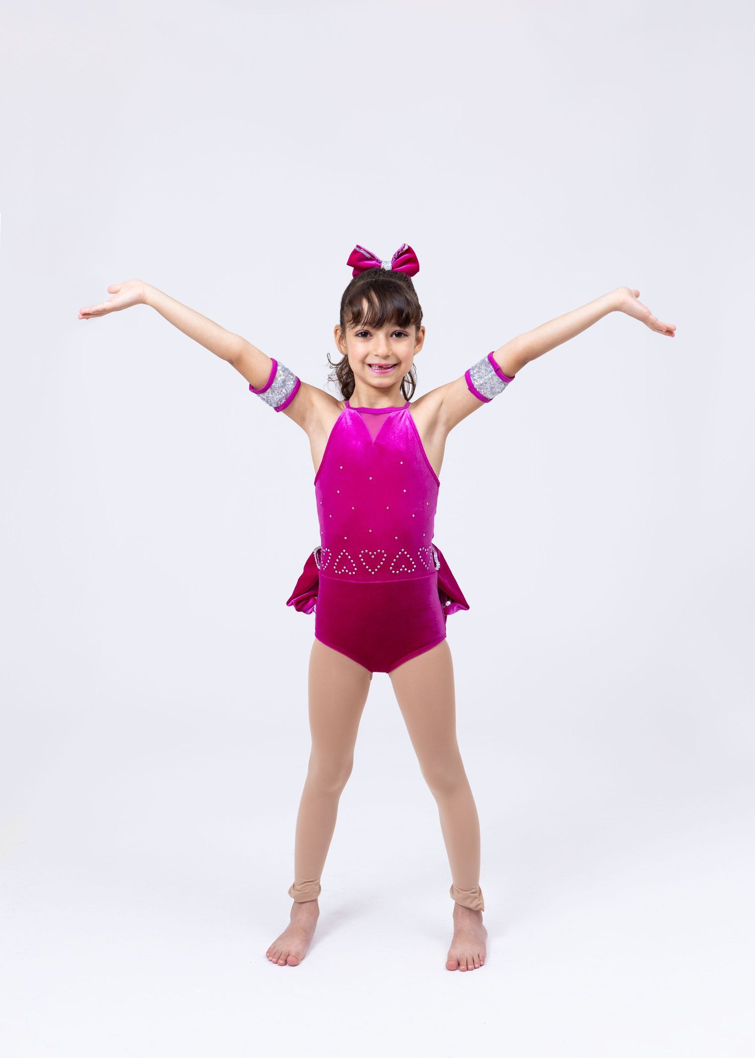 Young girl in hot pink gymnastics leotard with bow poses with arms raised in dance position.