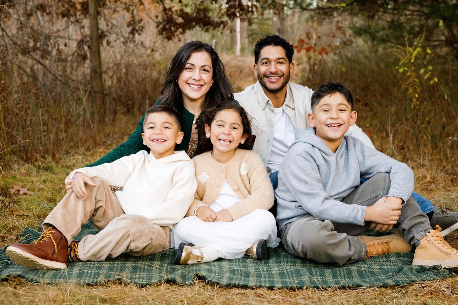 Happy Hispanic family of five smiles together on a plaid blanket outdoors in autumn.