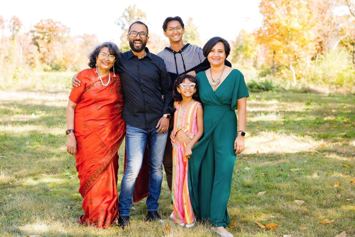 A happy South Asian family of five posing together outdoors in a park during autumn.