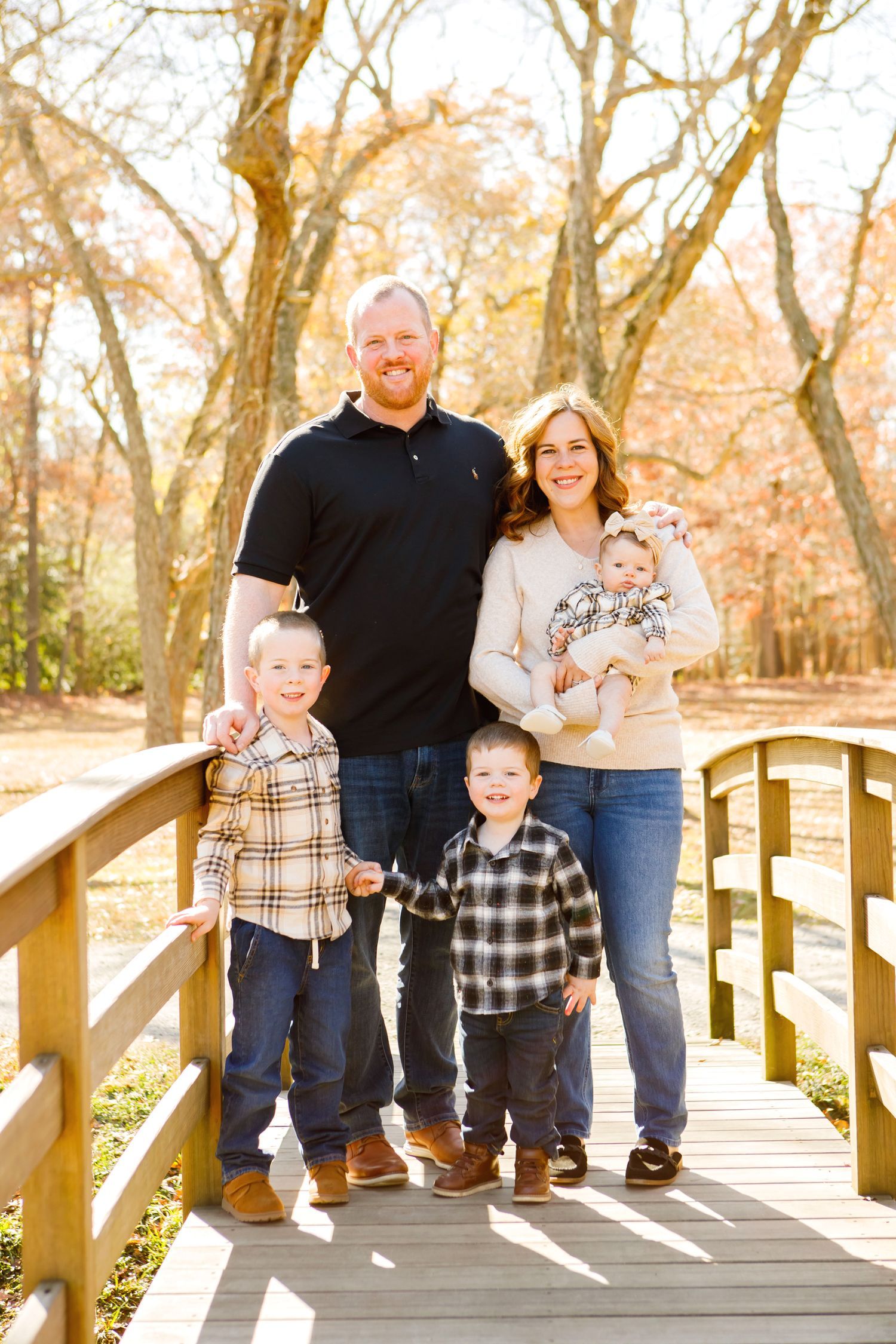 Family of five on wooden bridge in autumn park, parents with three young boys.