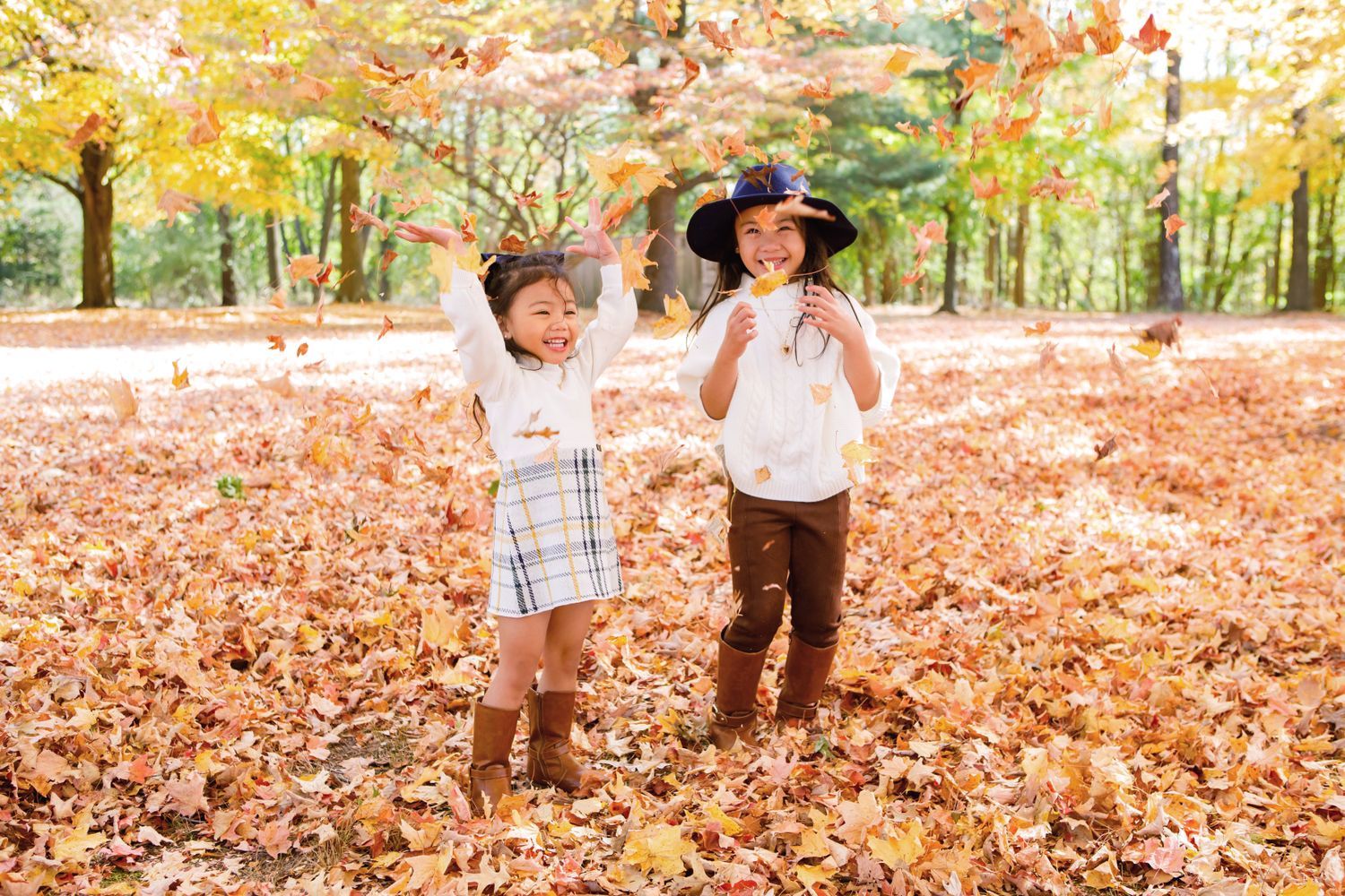 Two young children playing and tossing colorful autumn leaves in a vibrant fall forest.