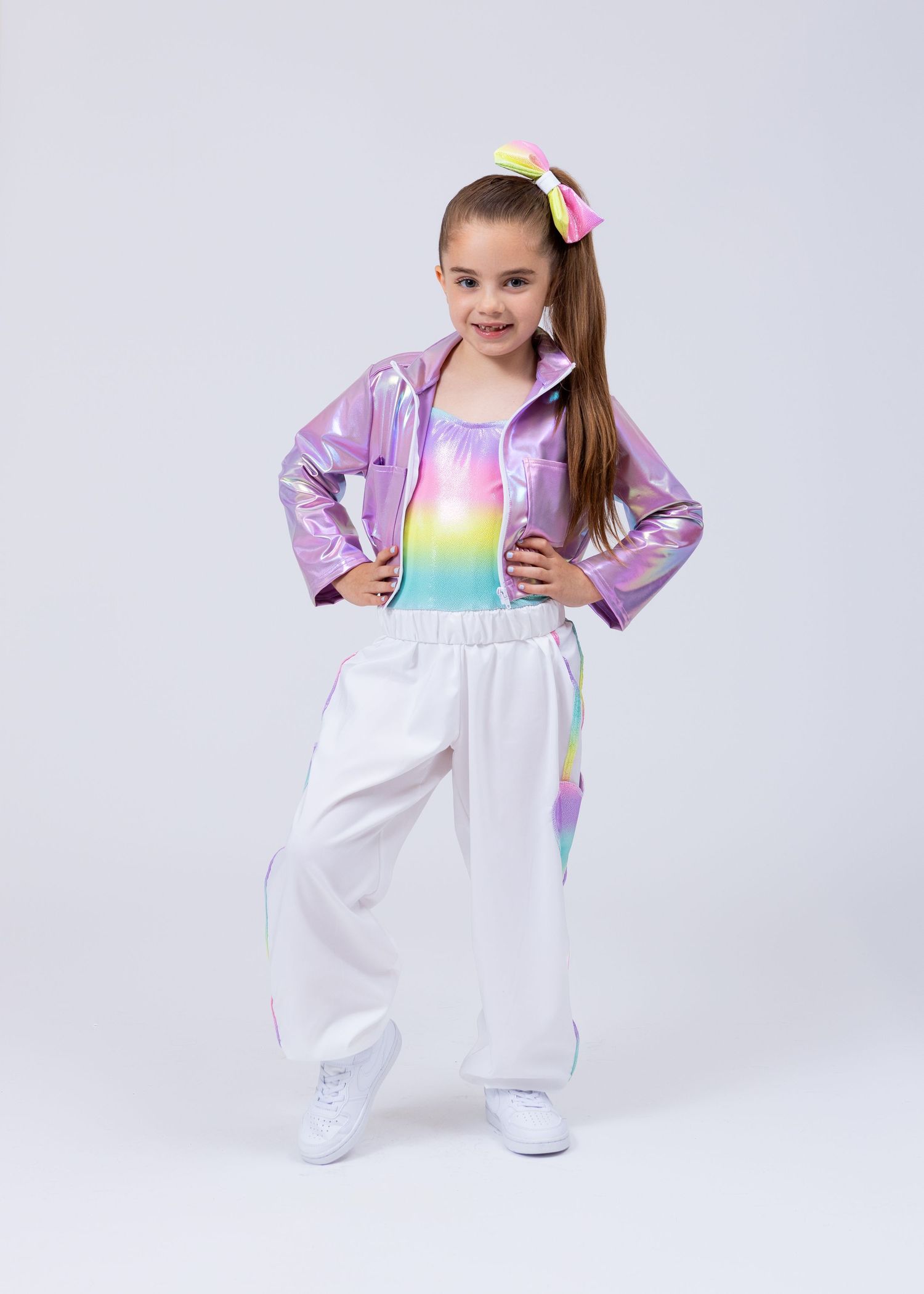 Young girl in iridescent purple jacket and rainbow outfit with white pants poses for dance photo.