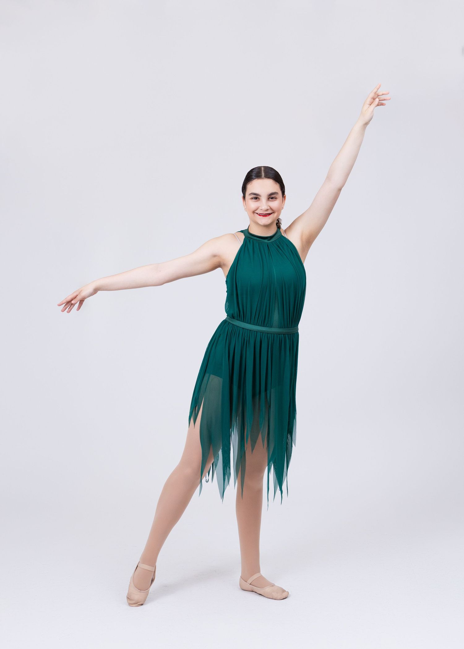 Teen dancer in green fringe halter dress performs elegant ballet pose on pointe.