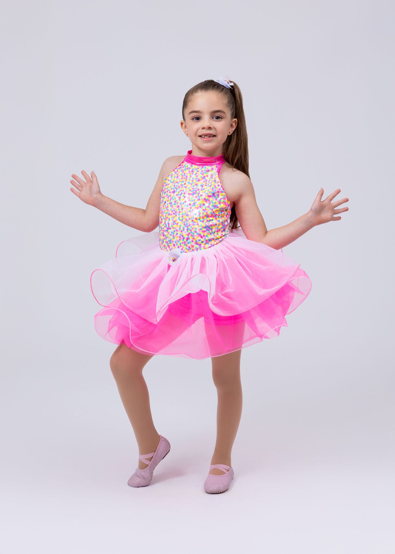 Young girl in pink sequin and tulle ballet dance costume poses with arms outstretched.