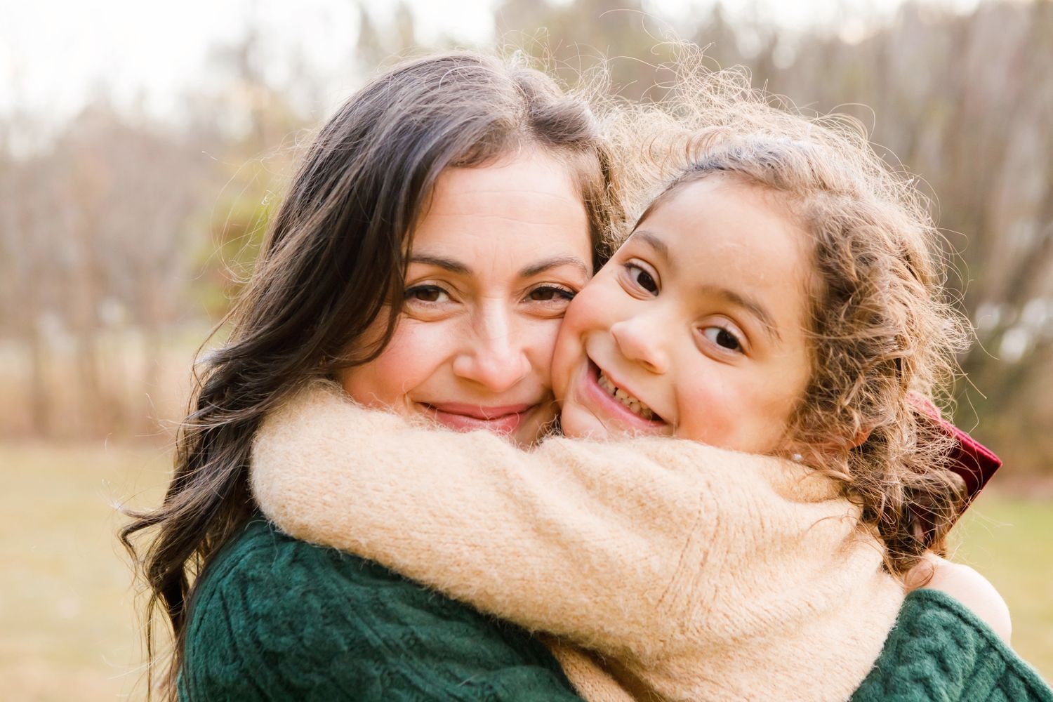 Mother and curly-haired daughter sharing a warm embrace outdoors.
