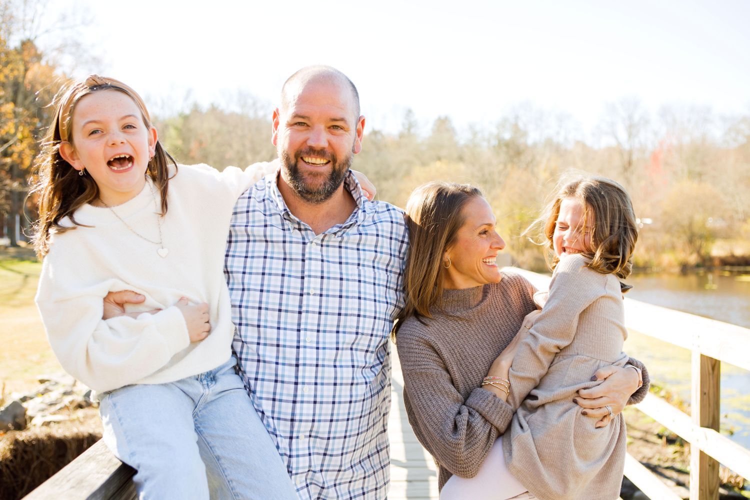 Happy family of four laughing outdoors with colorful fall trees in the background.