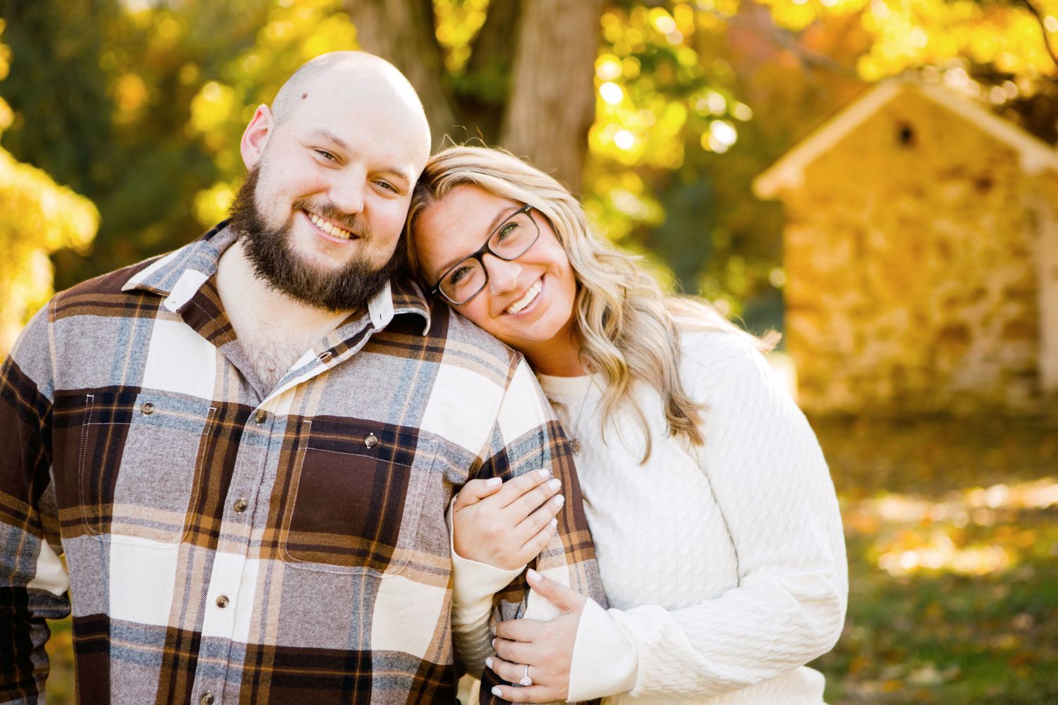 Couple smiling and embracing closely outdoors surrounded by warm fall colors.
