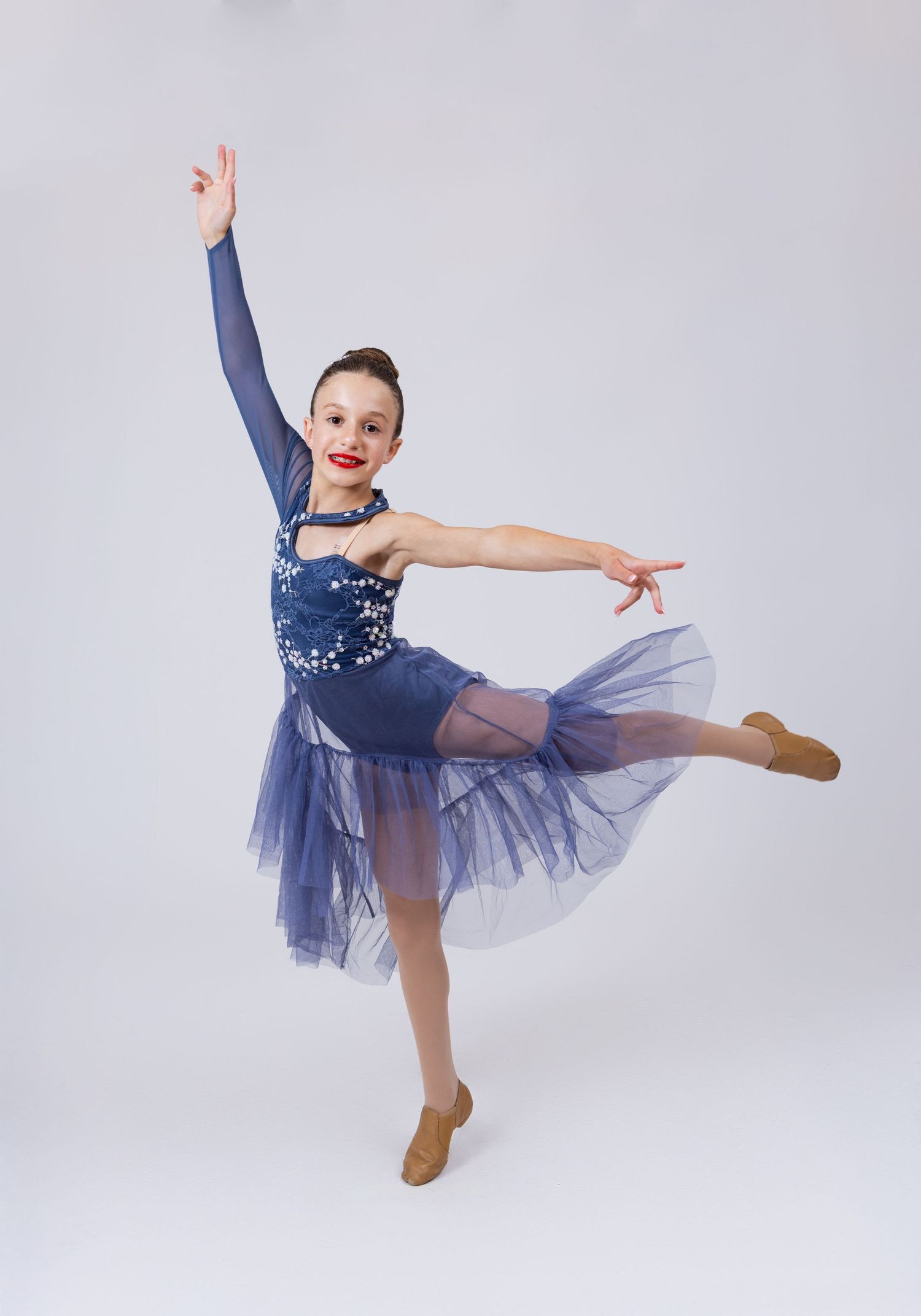 Young girl in blue sequin and tulle ballet dress performs an elegant arabesque dance pose.