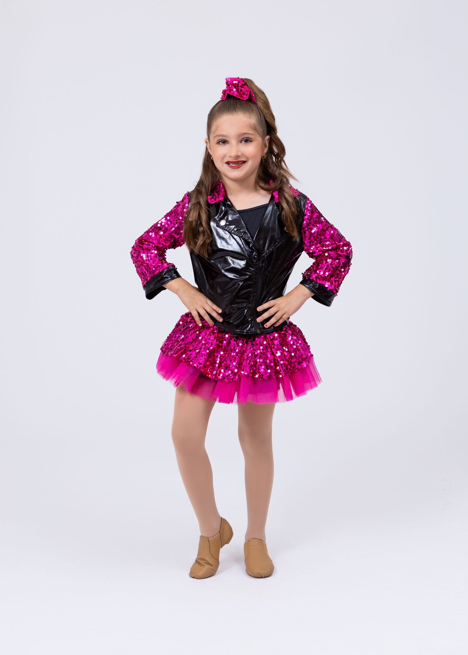 Young girl in pink sequin and black vinyl dance costume with tutu skirt poses confidently.