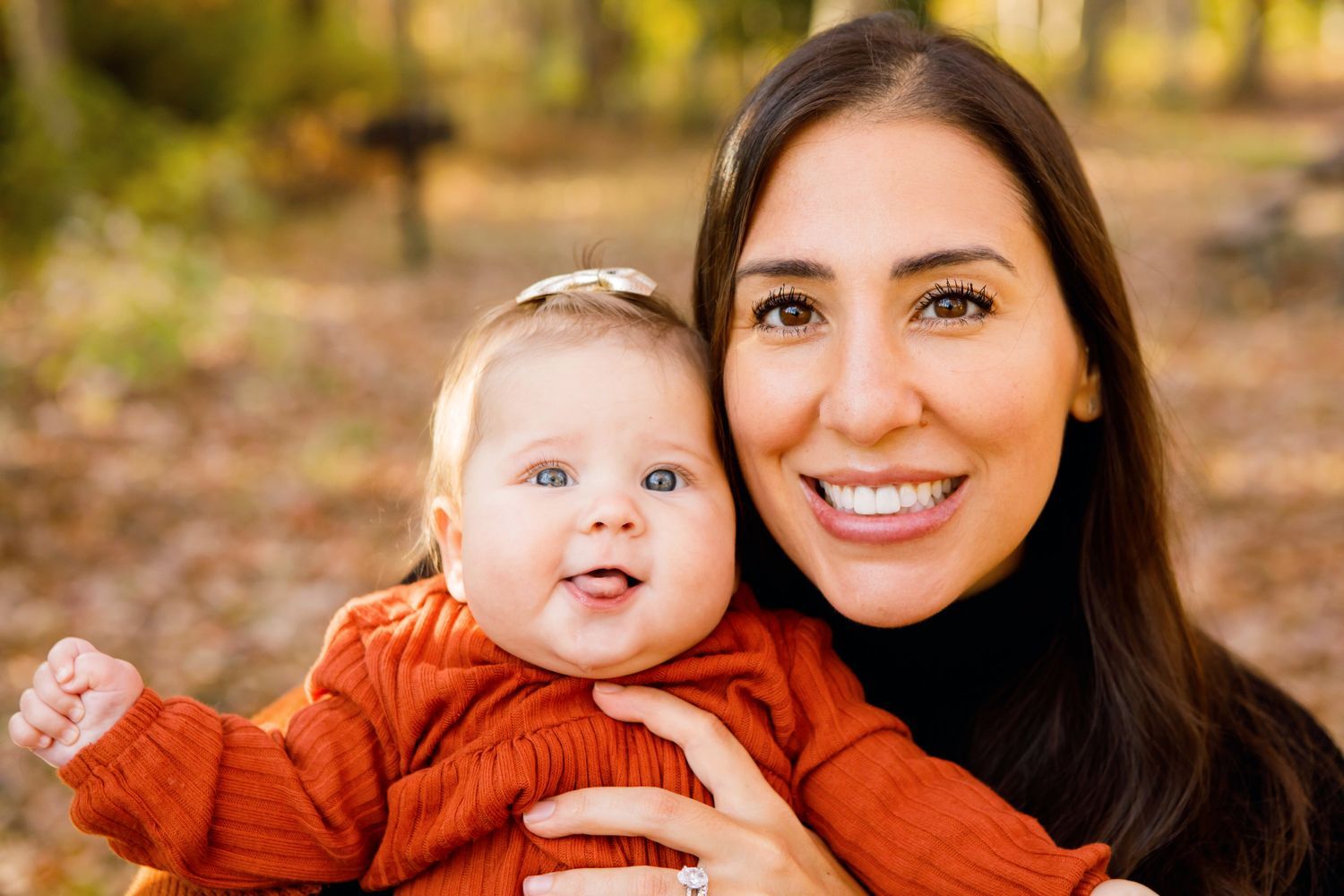 Smiling mother holding her happy baby girl outdoors in autumn setting.