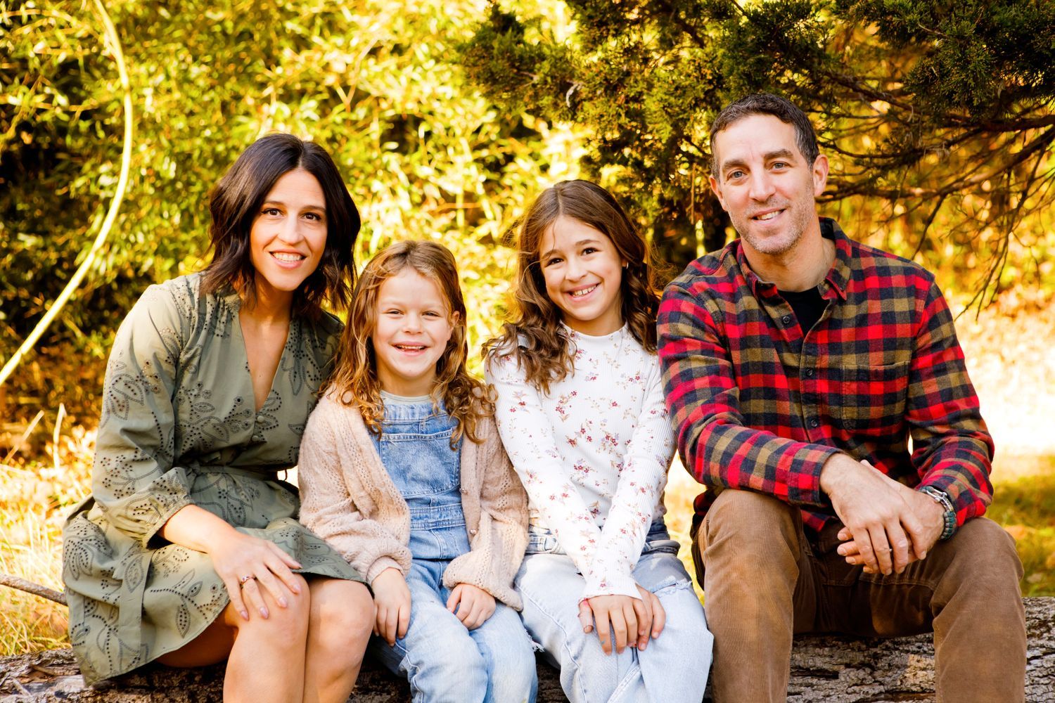 A happy family of four sitting together outdoors surrounded by golden autumn foliage.