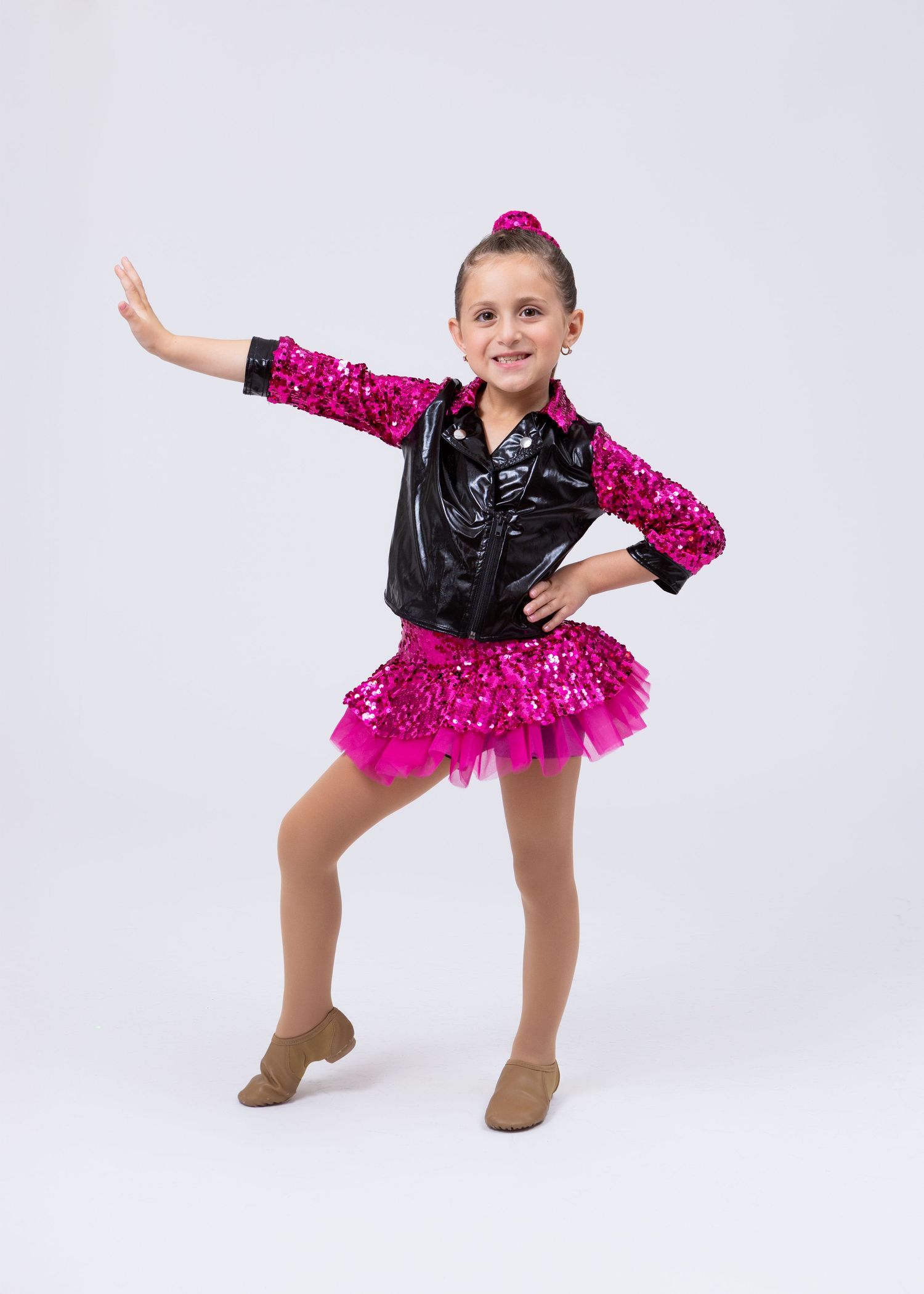 Young dancer in sequined pink skirt and black leather jacket strikes dynamic jazz dance pose.