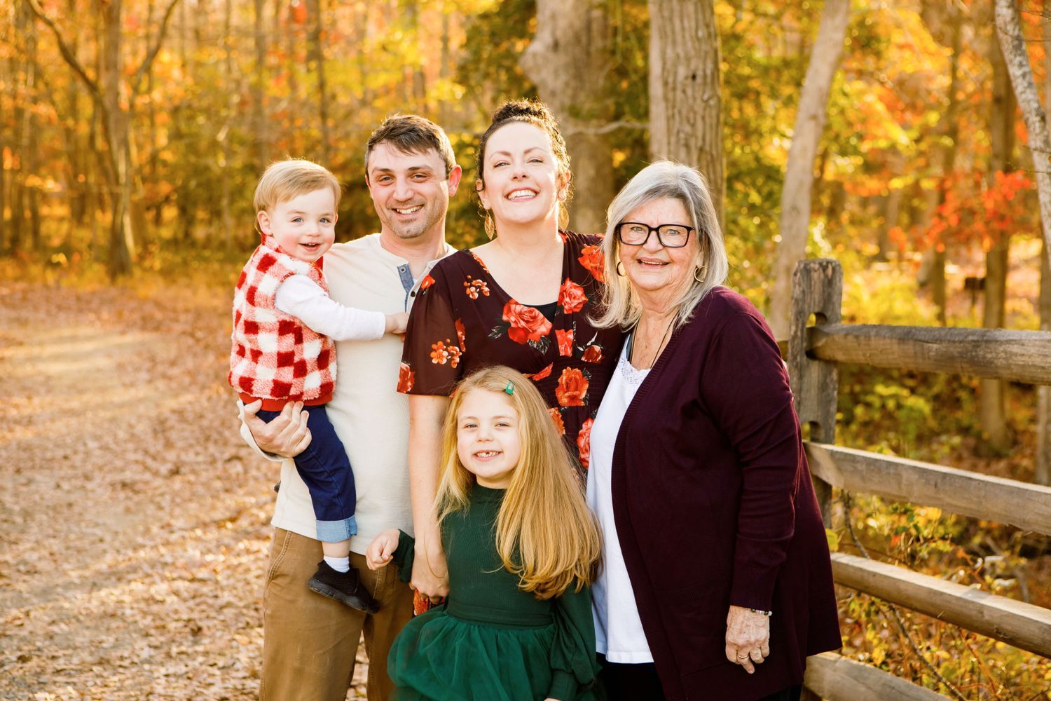 Three-generation family smiling together on an autumn forest path.
