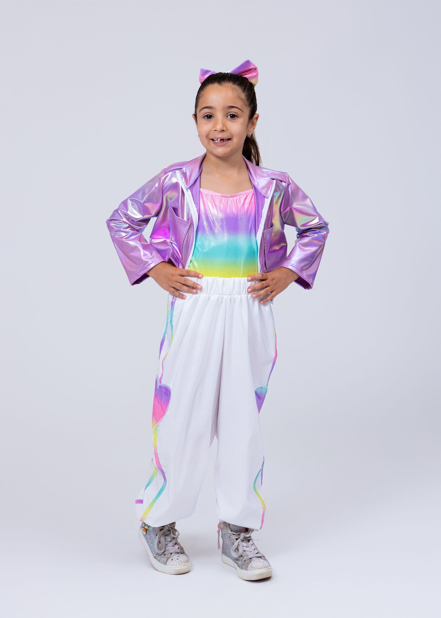 Young girl in iridescent purple jacket and rainbow outfit poses in a dance studio portrait.