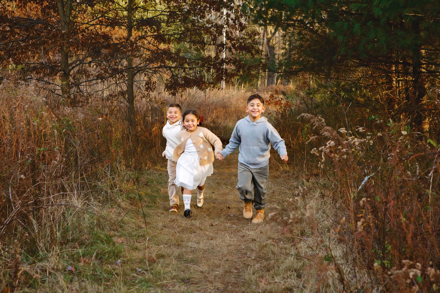 Three children running joyfully through an autumn forest trail surrounded by golden foliage.