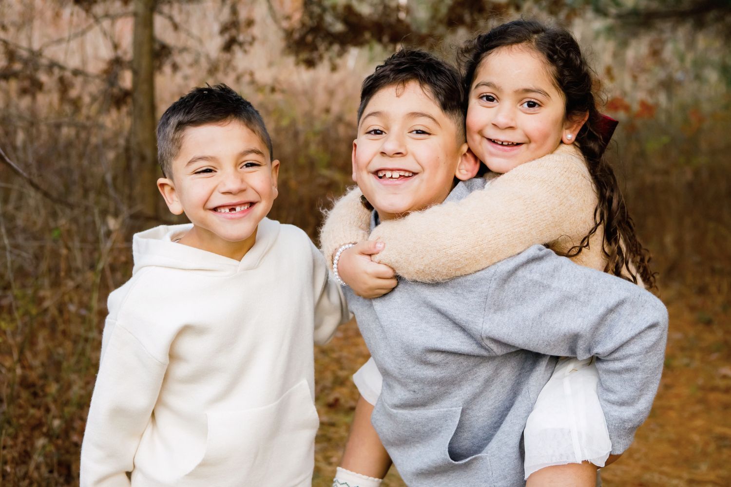 Three siblings hugging and smiling together in an outdoor fall photo session.