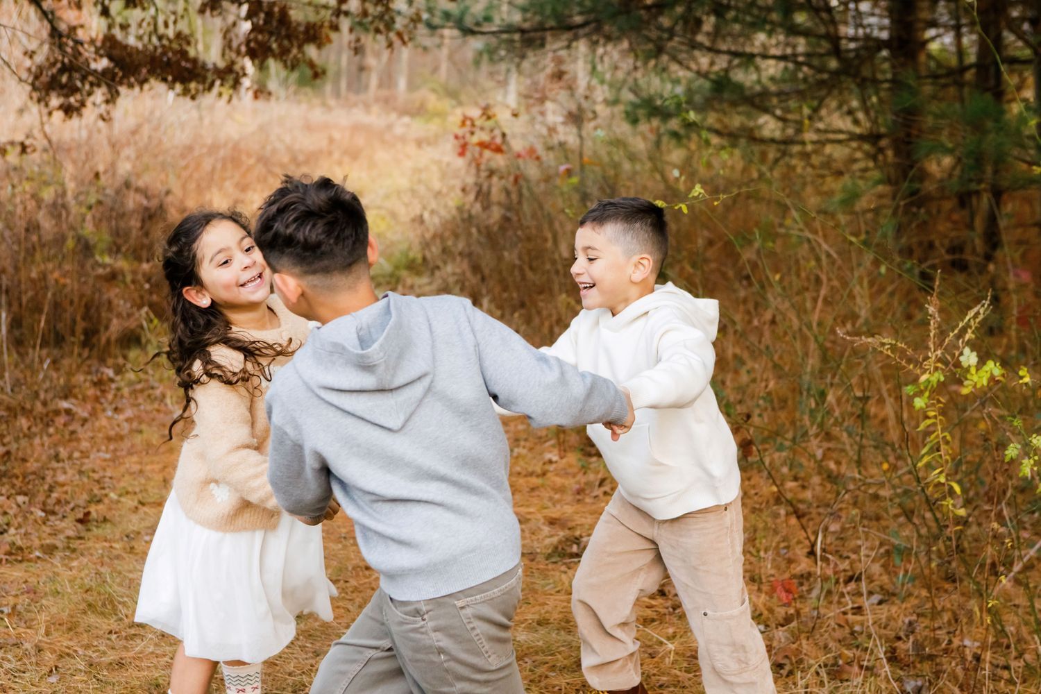 Children playfully interacting with their father outdoors among golden fall foliage.