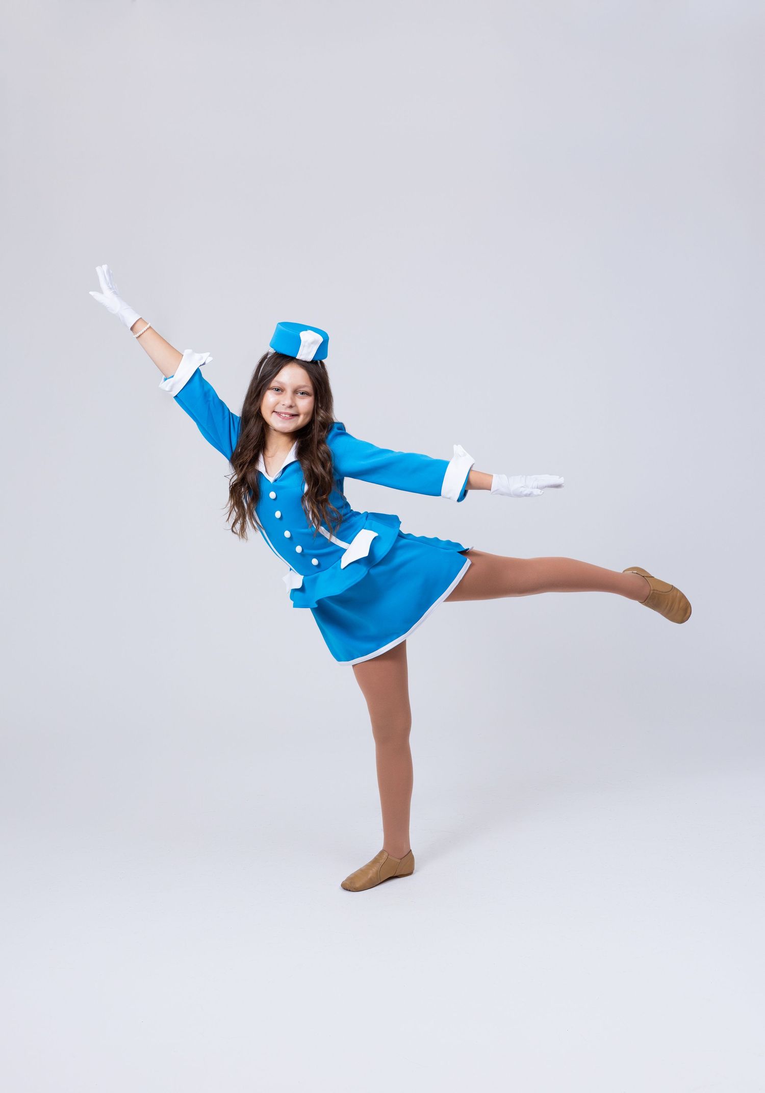 A young girl in a blue majorette costume with white gloves performs a high kick dance pose.