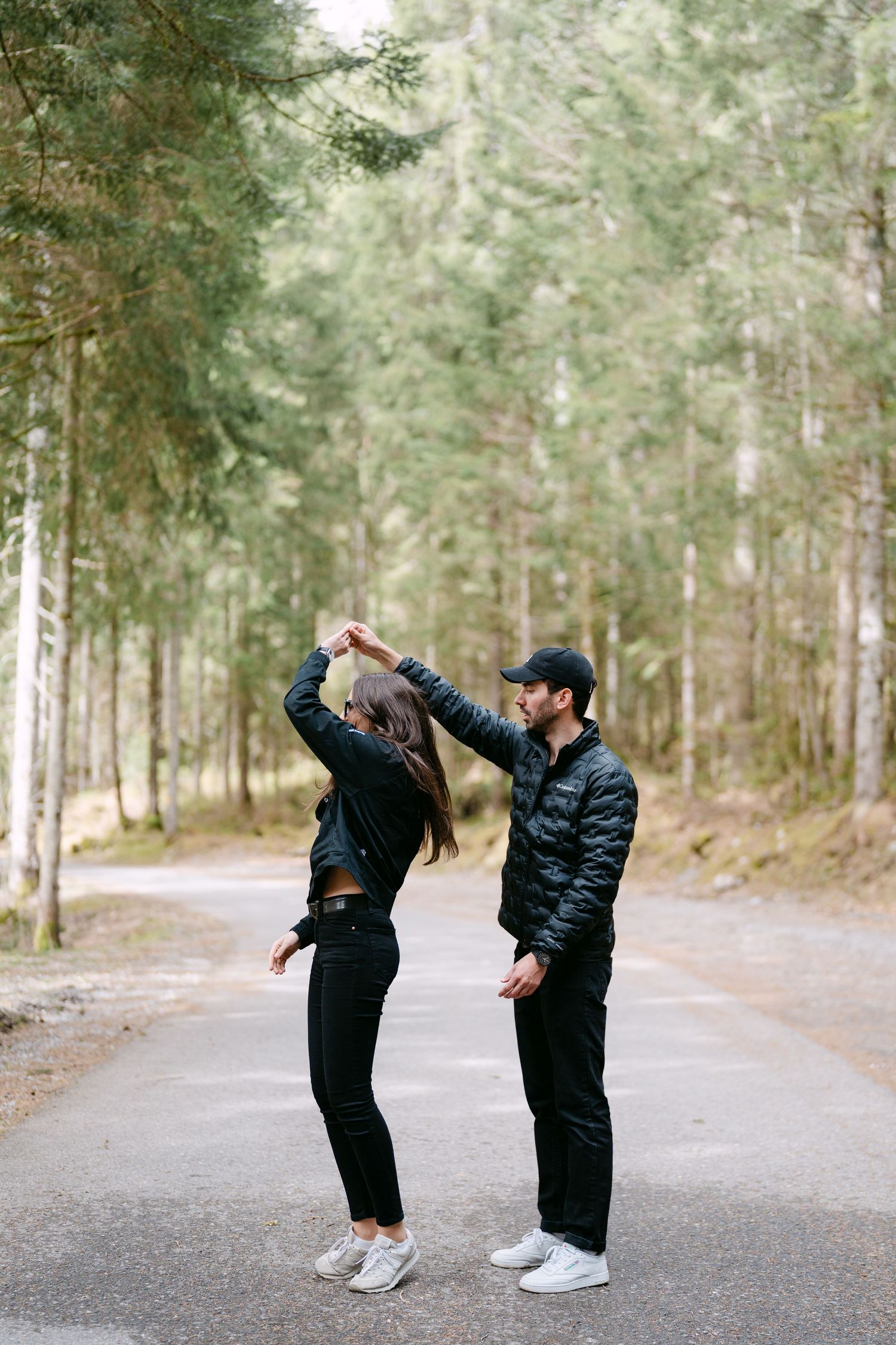 A playful sequence of dance moves on a forest path shows two people in black outfits.
