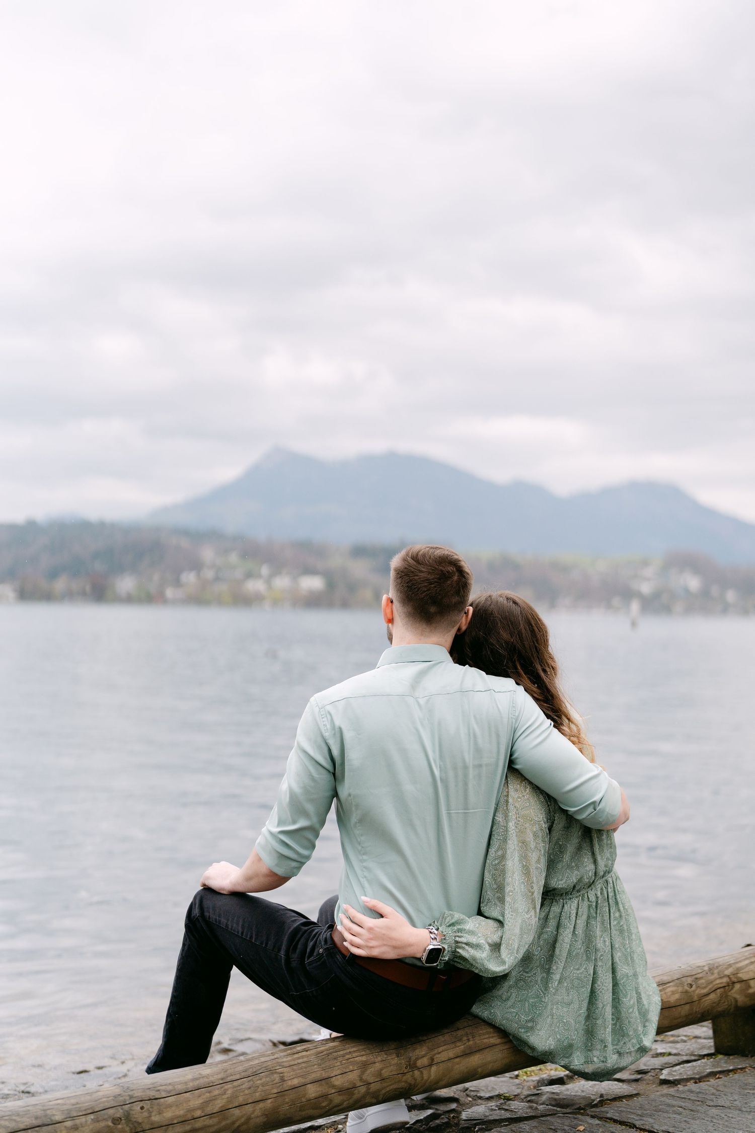 A couple sits together on a log overlooking a scenic mountain lake.