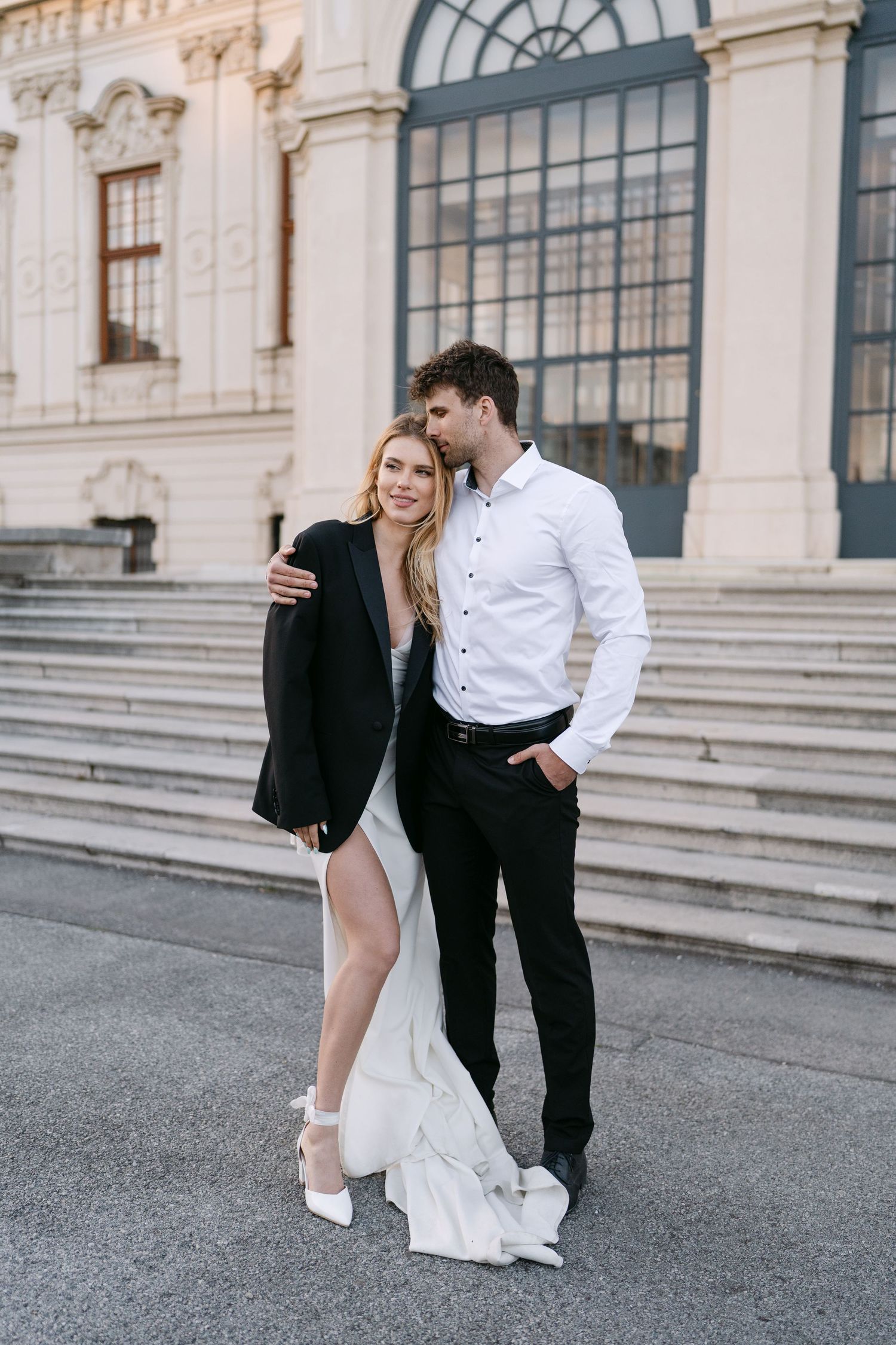 Fashionable couple posing on steps of a classical building in formal attire.
