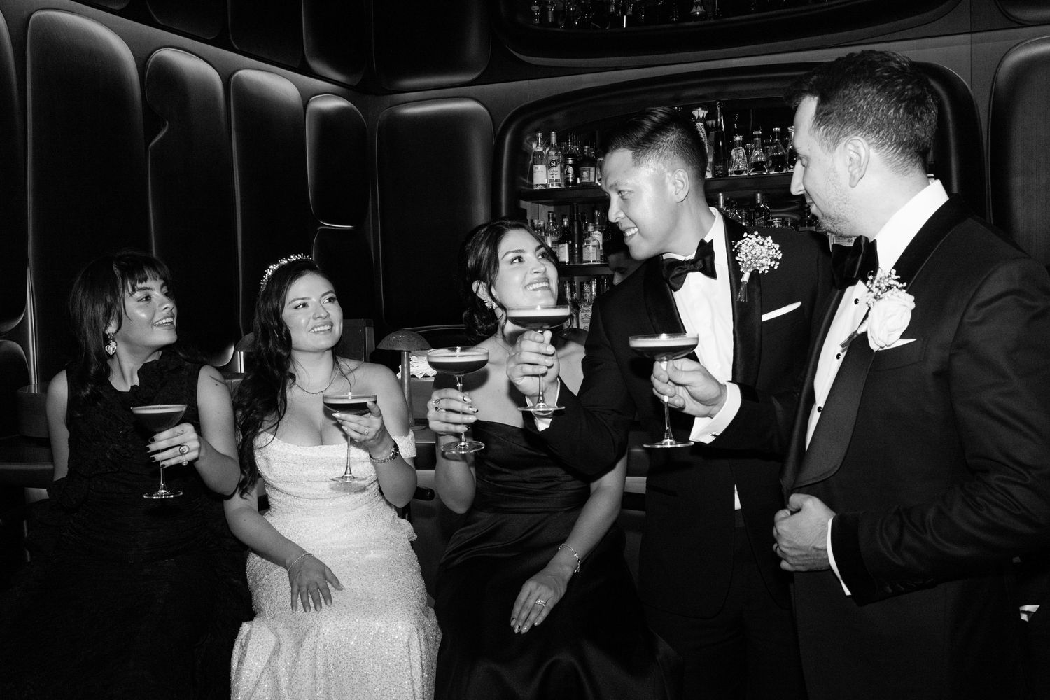 Wedding party enjoying cocktails and conversation at dimly lit luxury bar.