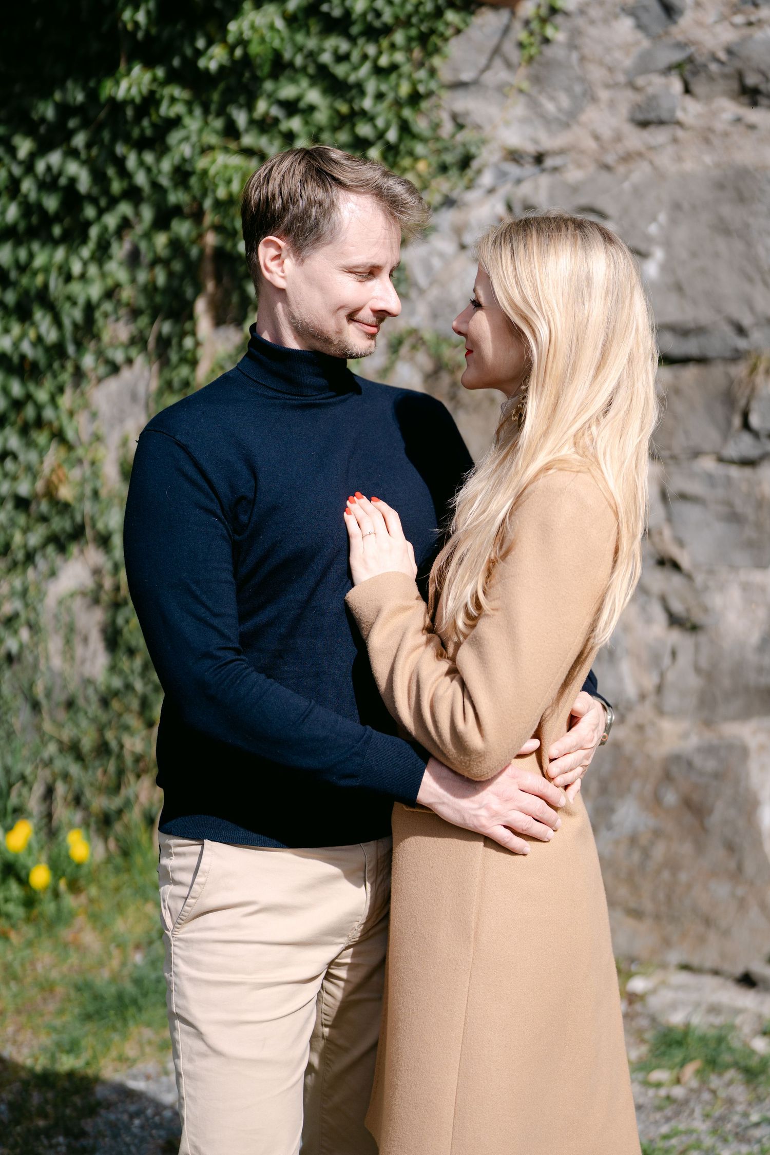 Joyful couple sharing laughs against stone wall backdrop in natural setting.